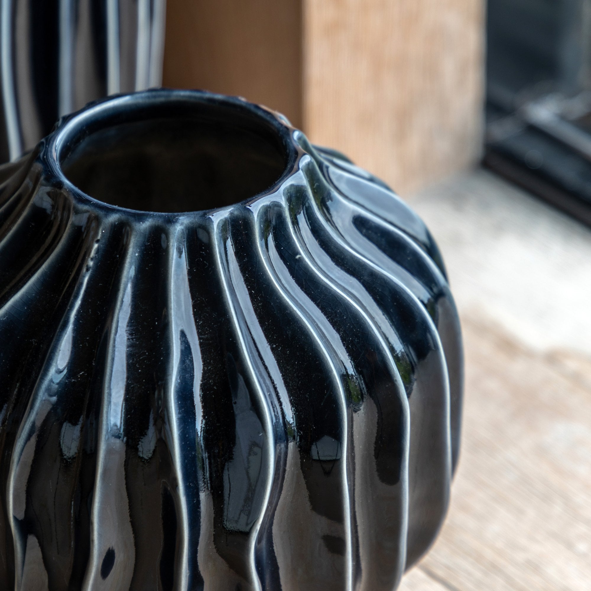 Close-up of a glossy black vase with a textured wavy pattern.