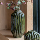 Tall dark green fluted vase with leaves in it. Also a smaller vase in the bottom right corner.