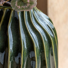 Top portion of a dark green fluted vase with leaves in it.