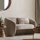 A beige two-seater sofa with an embroidered cushion in a living room setting.