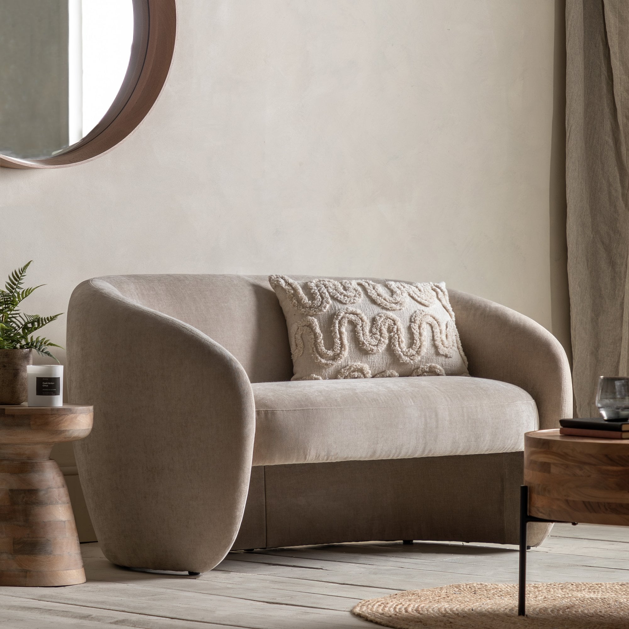 A beige two-seater sofa with an embroidered cushion in a living room setting.