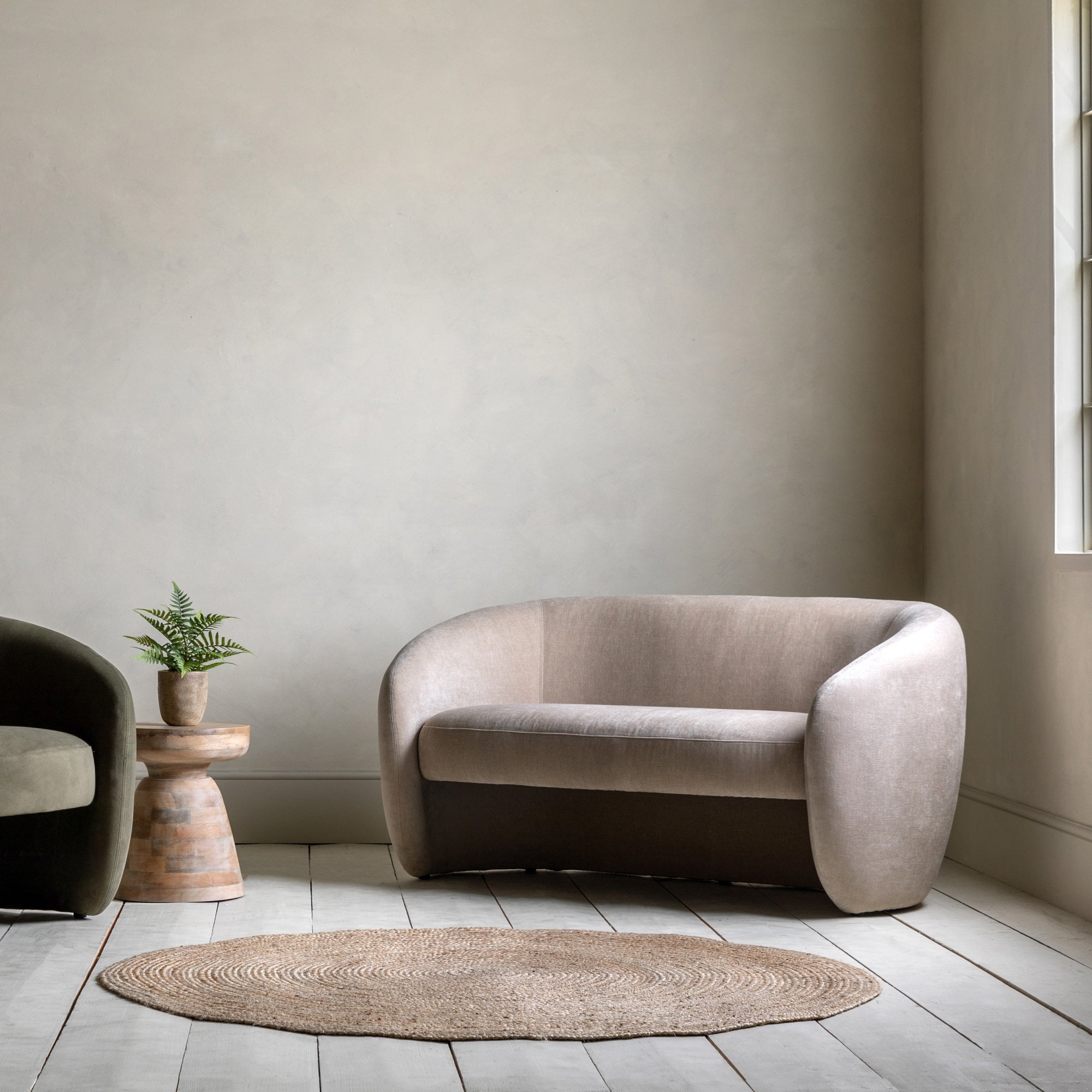 A beige two-seater sofa in a minimalist room with a rug and wooden side table.