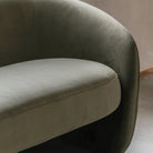Detail shot of the curved armrest and seat cushion of the sage green velvet sofa.