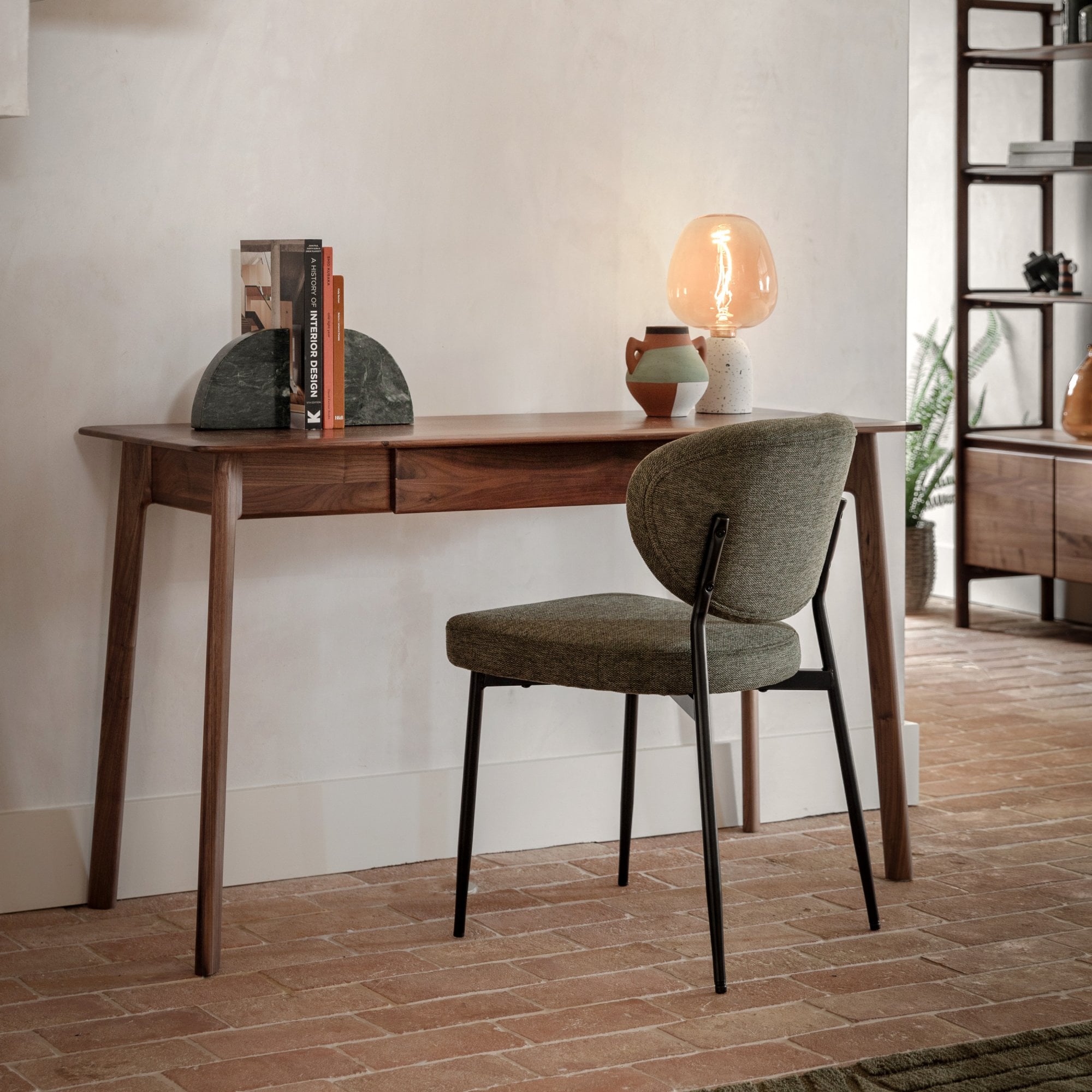 A sleek wooden desk with a green chair, illuminated by a warm table lamp, creating a cozy study.
