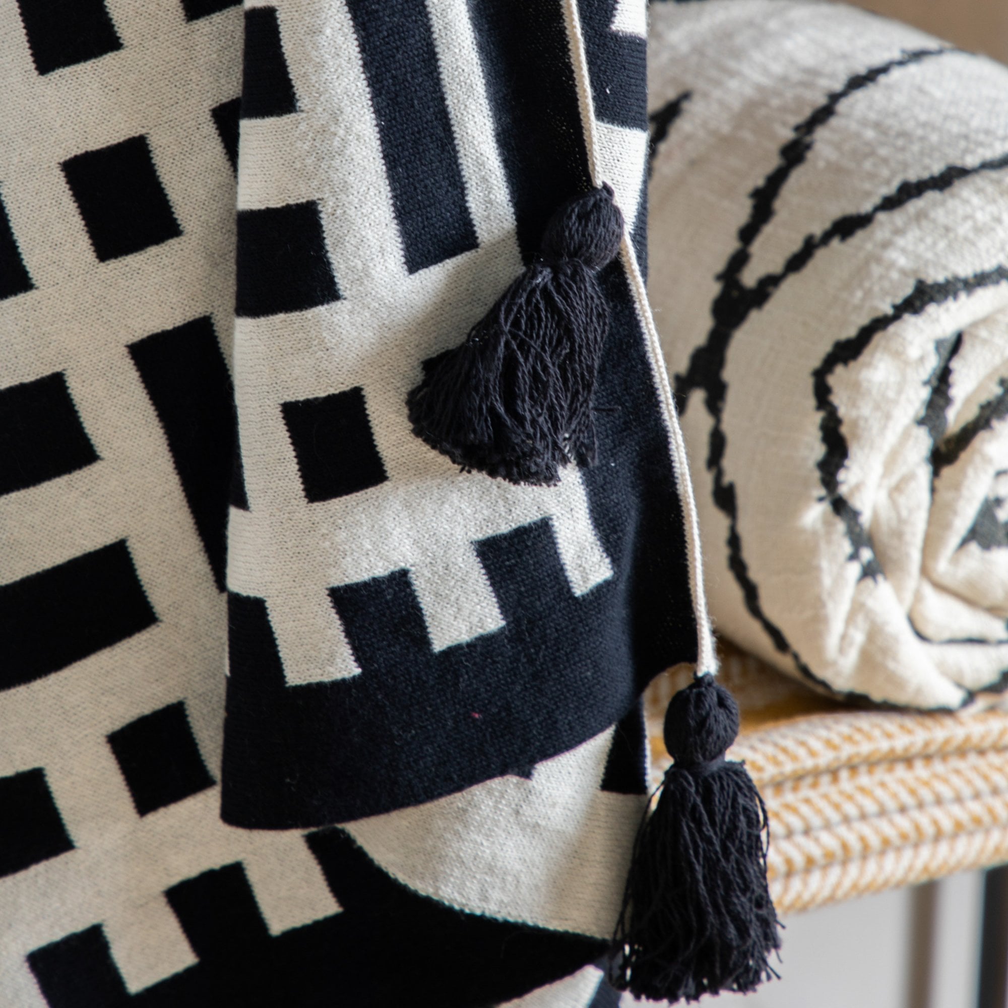 Close-up of a throw with black tassels and a white and black geometric pattern.