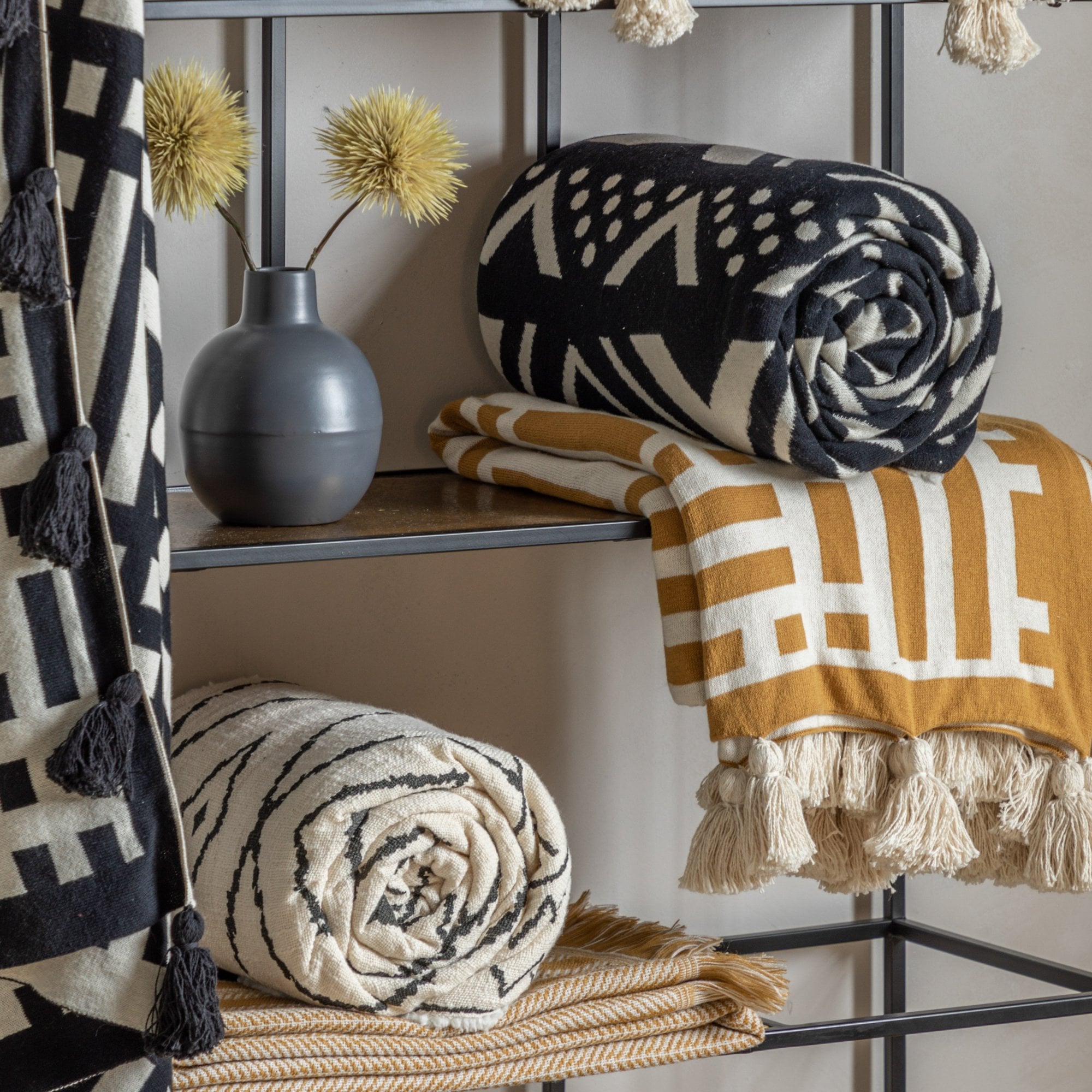 Shelves displaying various rolled throws with tribal and geometric patterns, and decorative vases.