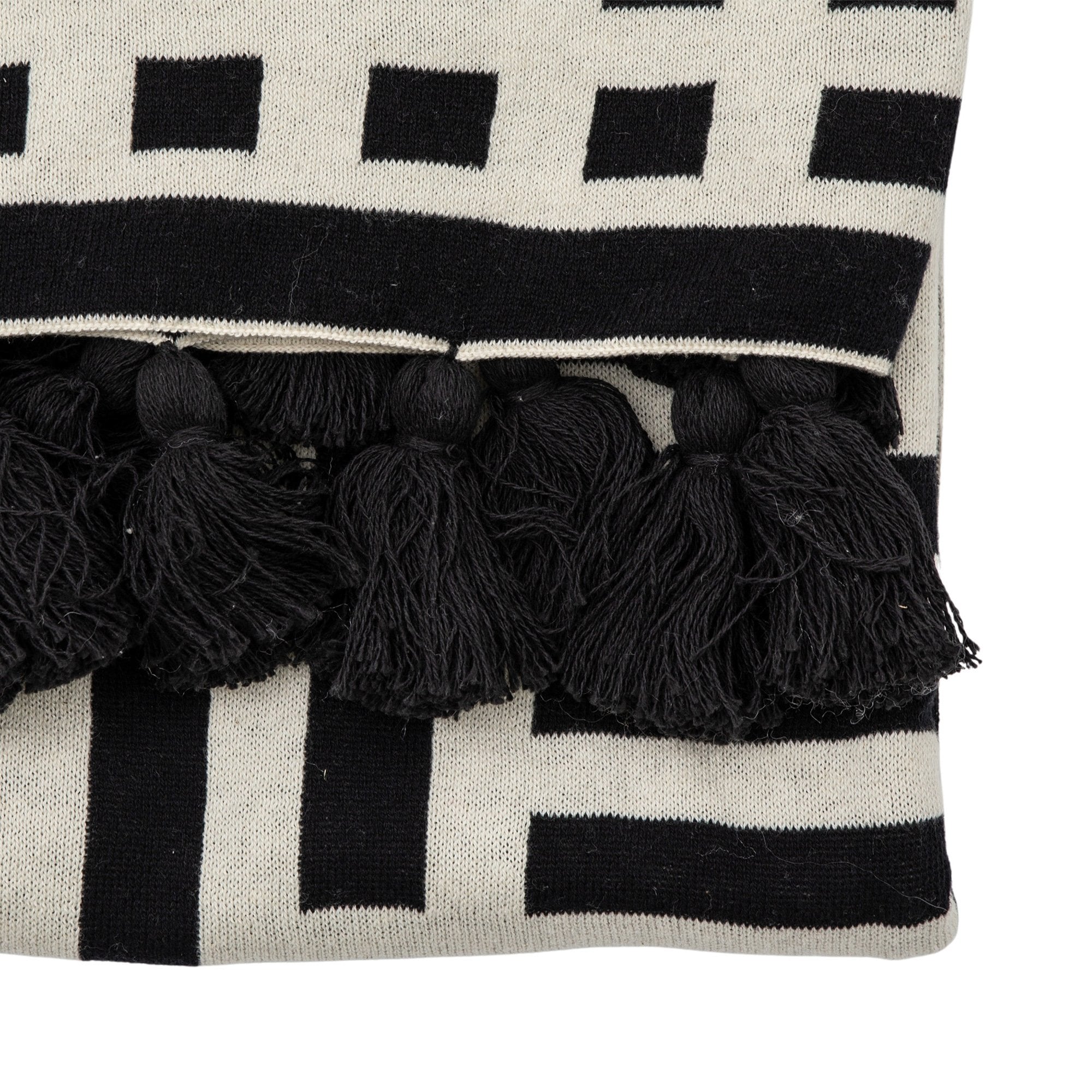 Close-up of black tassels on a patterned black and white throw.