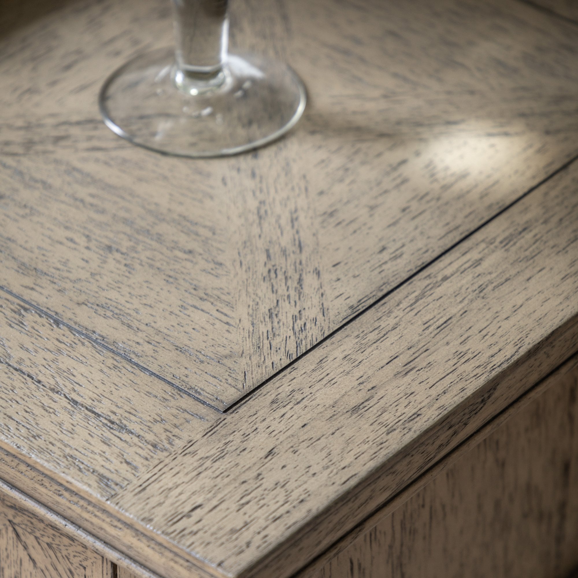 Close-up of the tabletop with a geometric patterned wood grain and a glass.