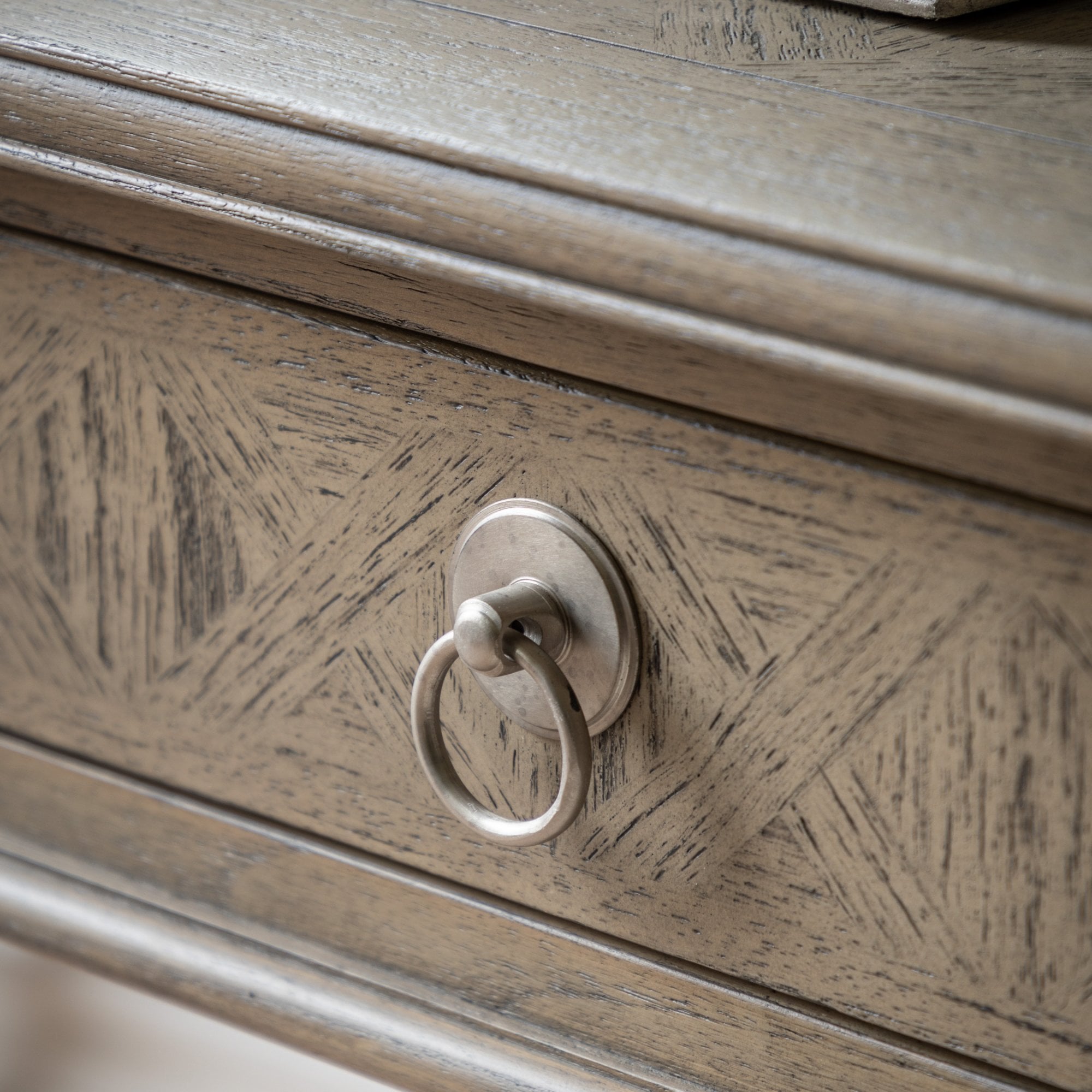 Close-up of a drawer with a geometric patterned wood grain and a ring pull handle.