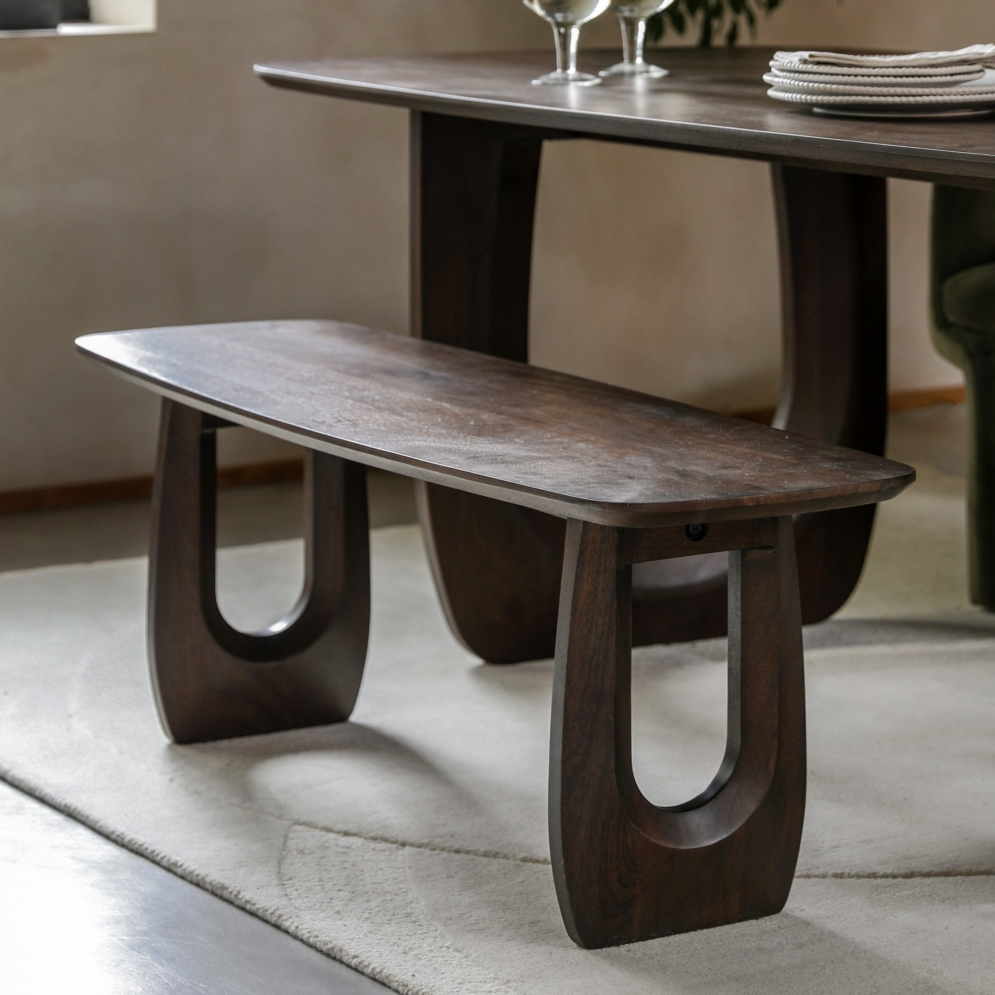 A minimalist dark wood dining bench with a dining table in the background.