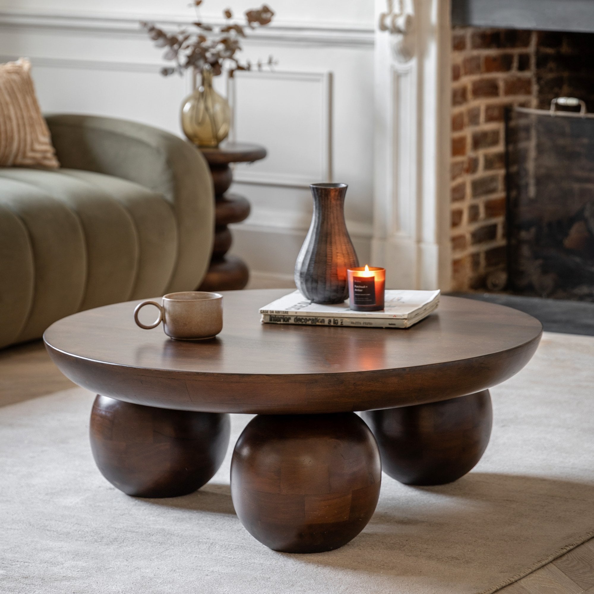A round wooden coffee table with spherical legs, styled with a mug, vase, and candle.