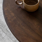 Close-up of a dark wooden round coffee table surface with a light brown mug.