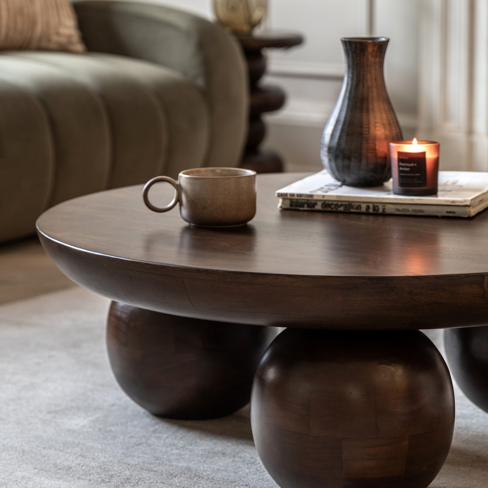 Round wooden coffee table with spherical legs, holding a mug, vase, and lit candle.