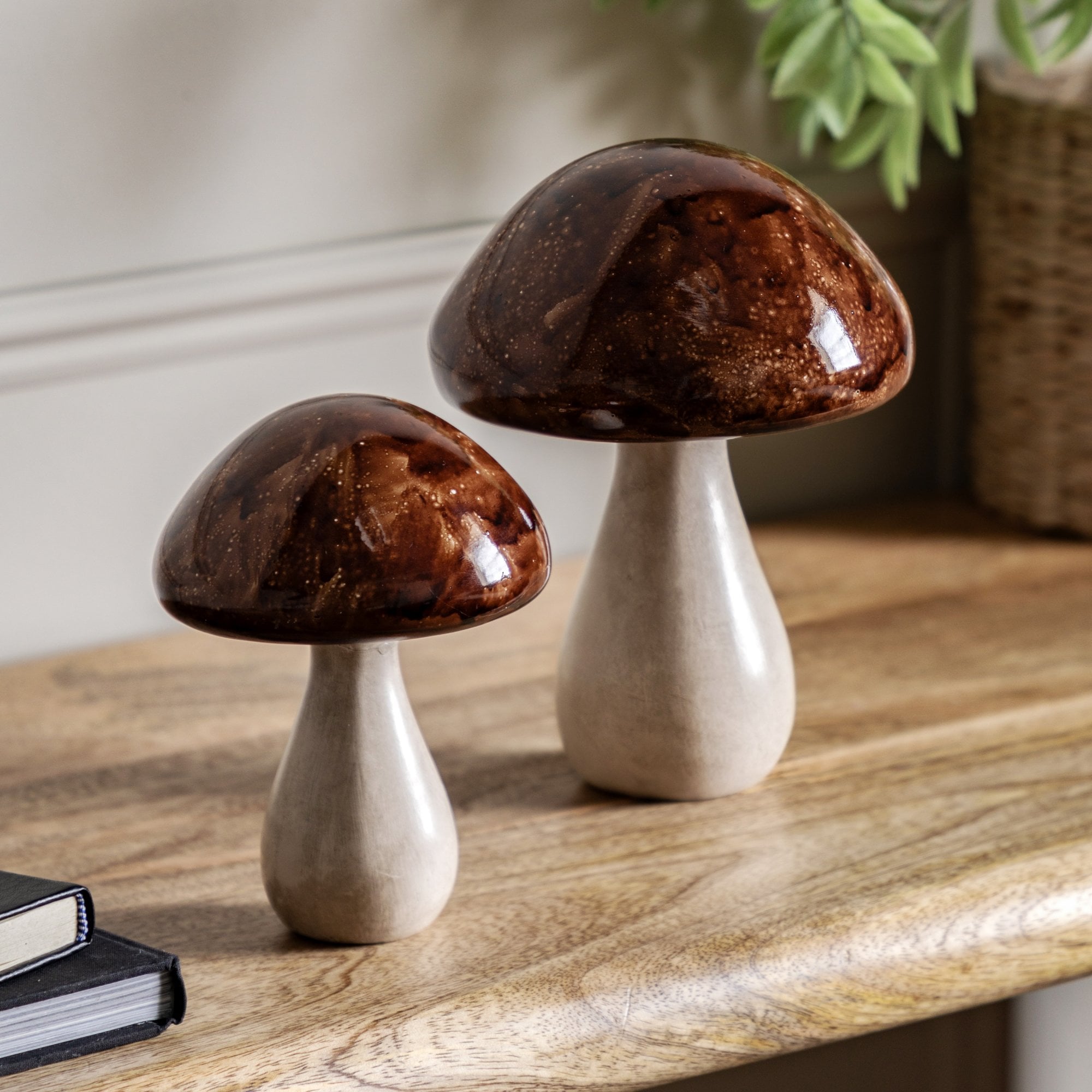 Two decorative mushroom ornaments on a wooden table with a plant in the background.