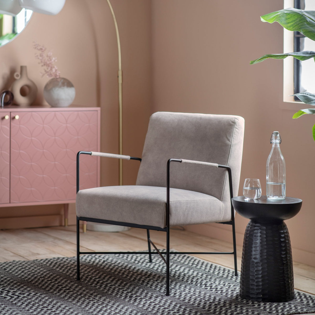 A beige armchair with black metal frame sits on a rug in a stylish living room.