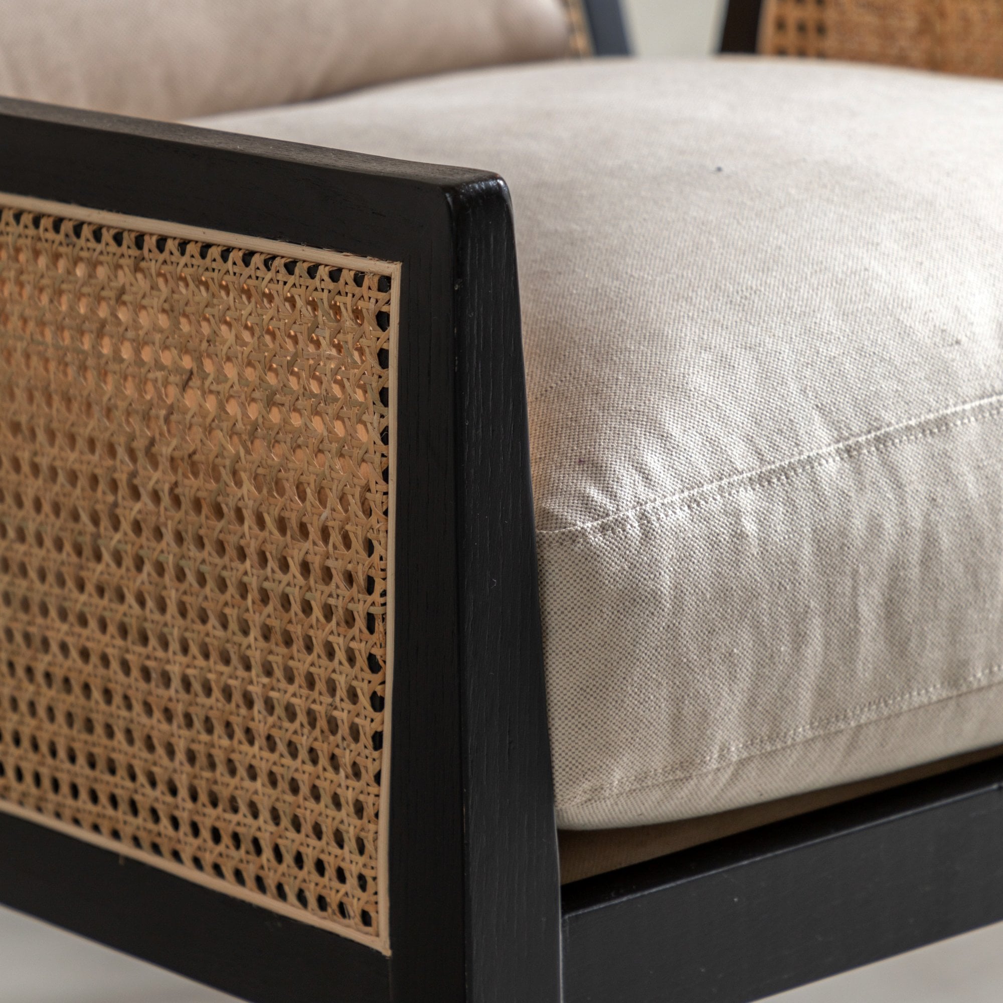 Close-up of the armchair showing the black wooden frame, cane weaving, and light cushion.