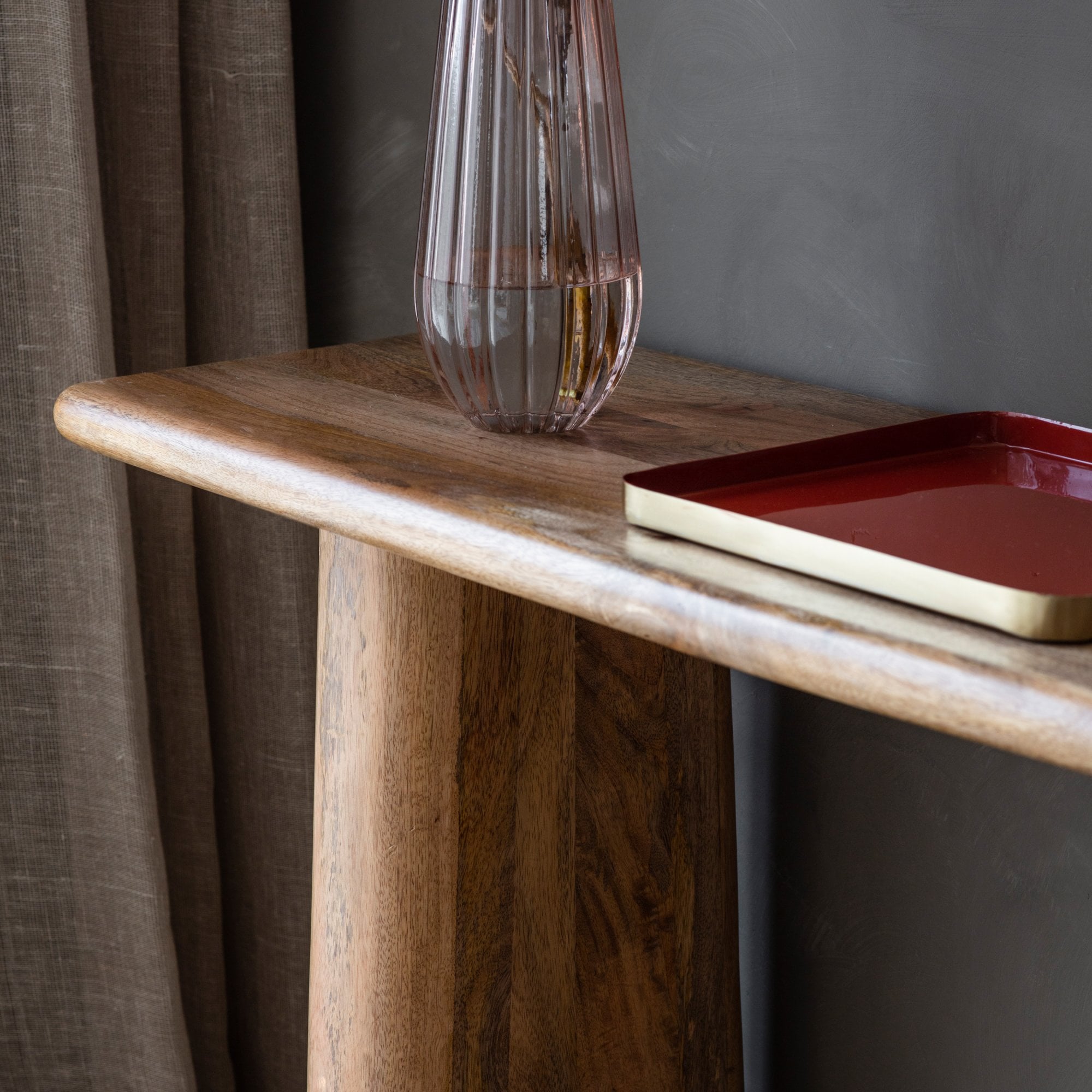 Close-up of a rustic mango wood console table with a ribbed glass vase.