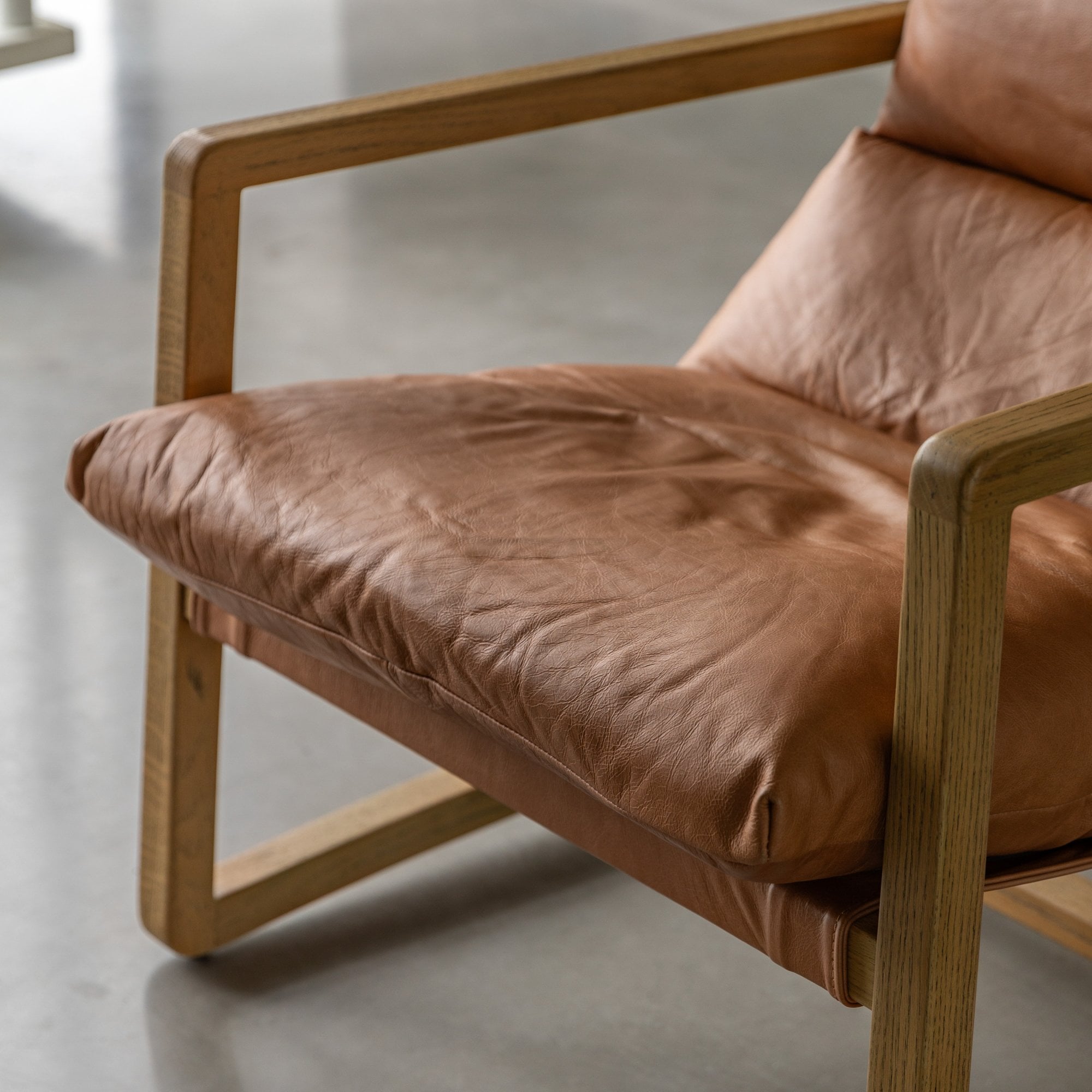 Close-up of the tan leather seat cushion and wooden armrest of an armchair.