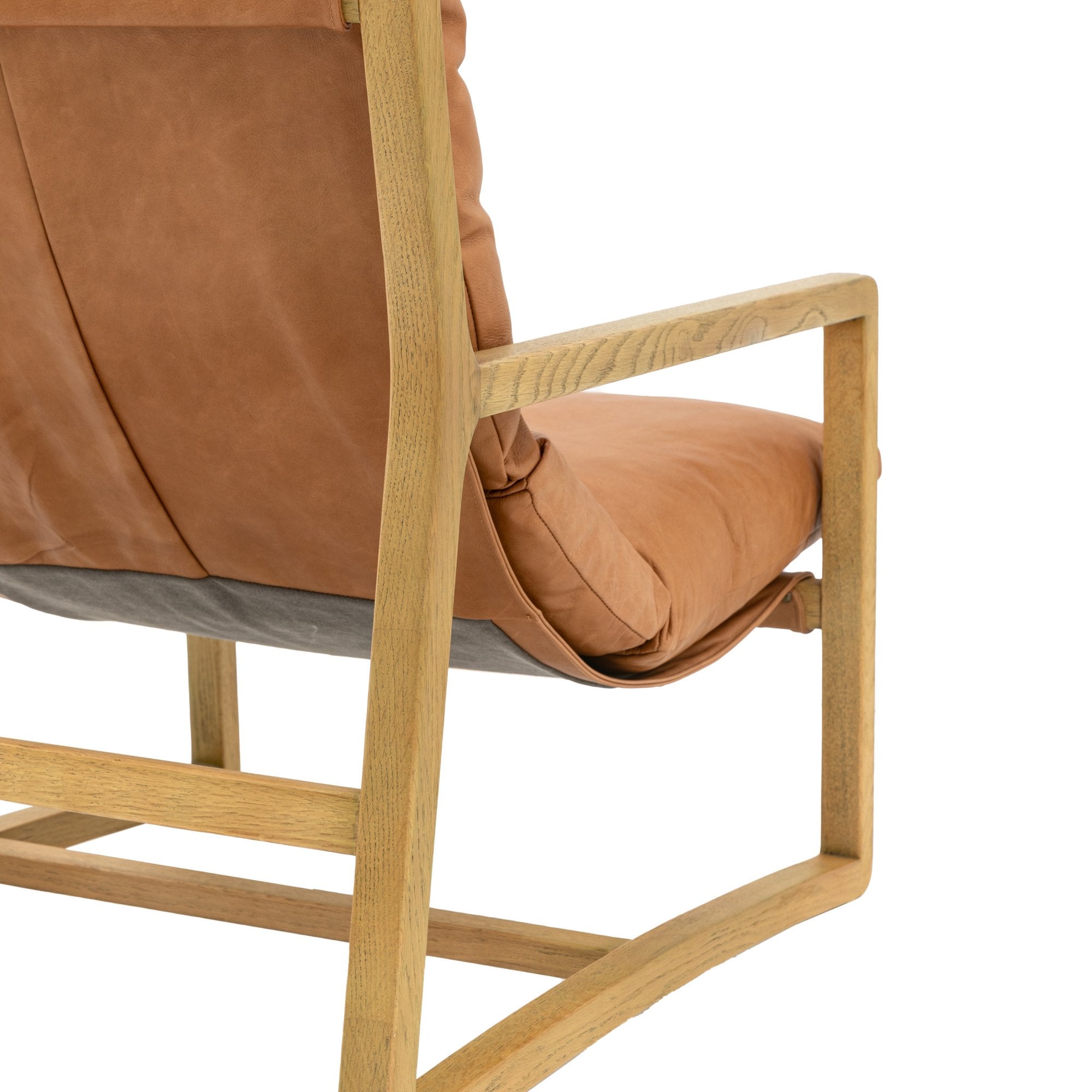 Detail of the tan leather cushion and wooden frame of the armchair's armrest.