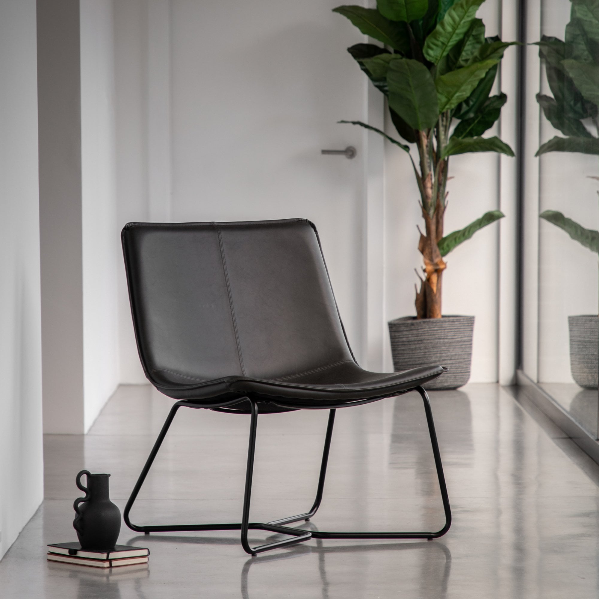 Black leather lounge chair with metal frame in a modern hallway with a plant.