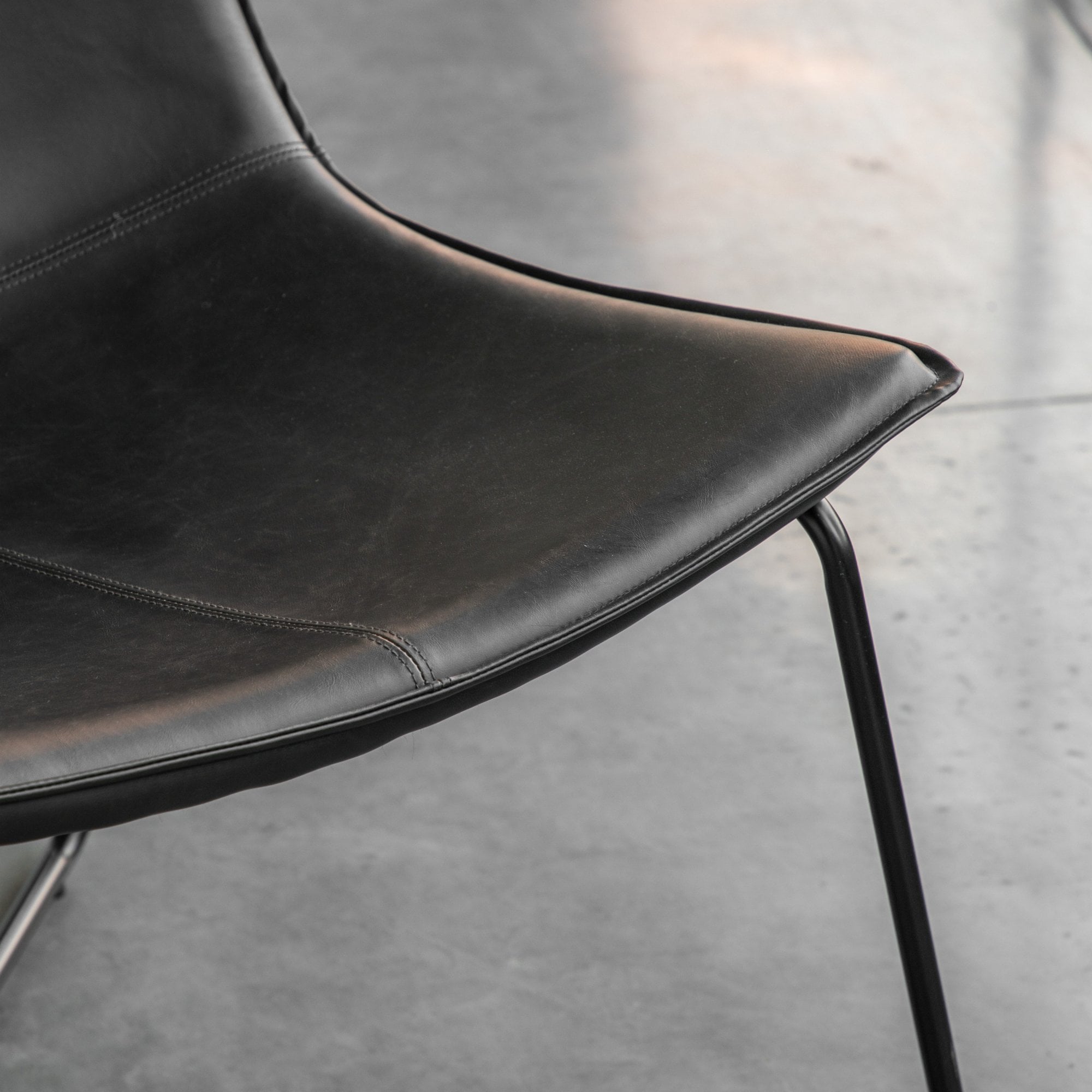 Close-up of the curved black leather seat and armrest of a lounge chair.