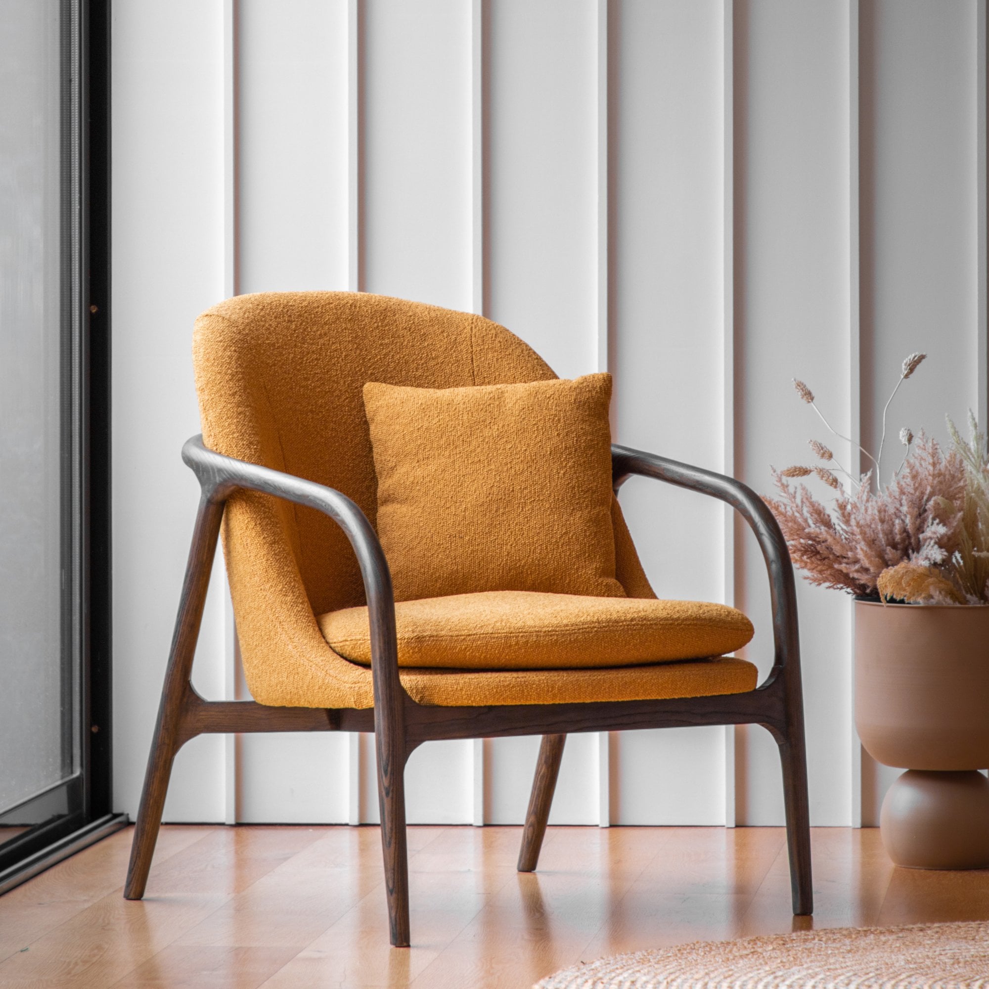 A mustard yellow accent chair with a dark wooden frame and a matching cushion sits in a modern room.