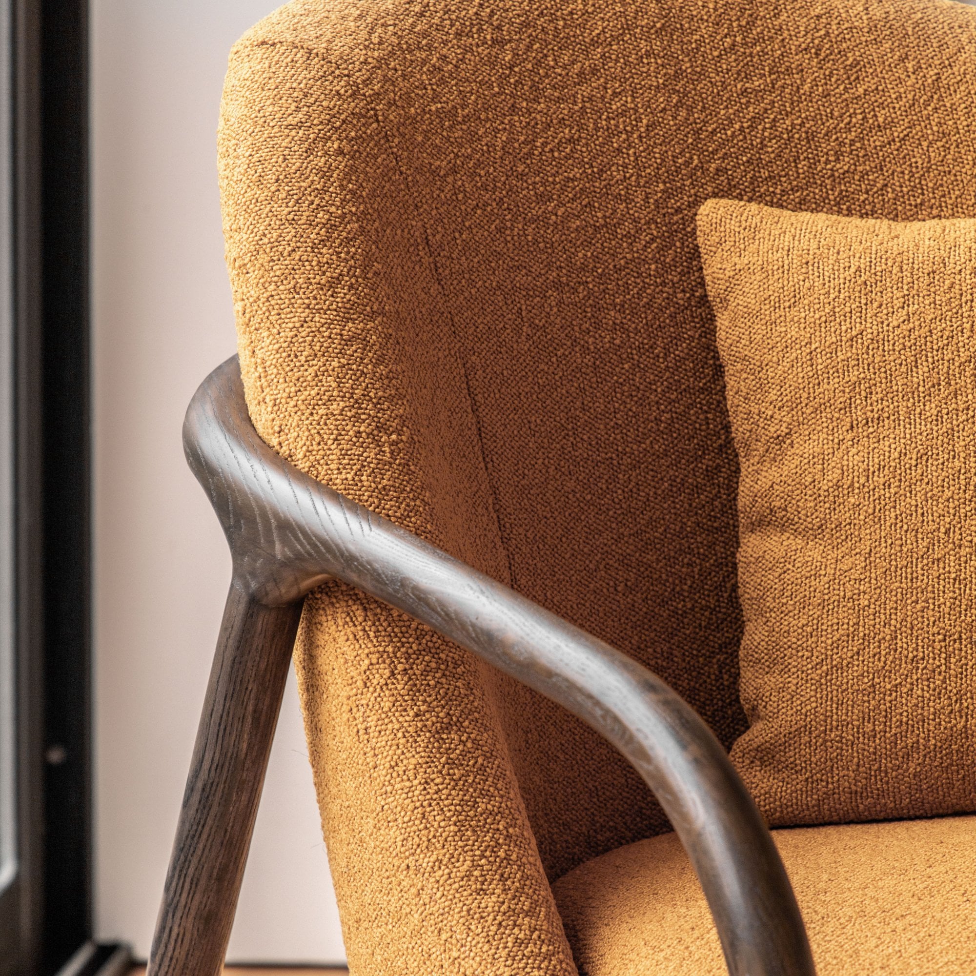 Close-up of the mustard yellow fabric and dark wooden armrest of an accent chair.