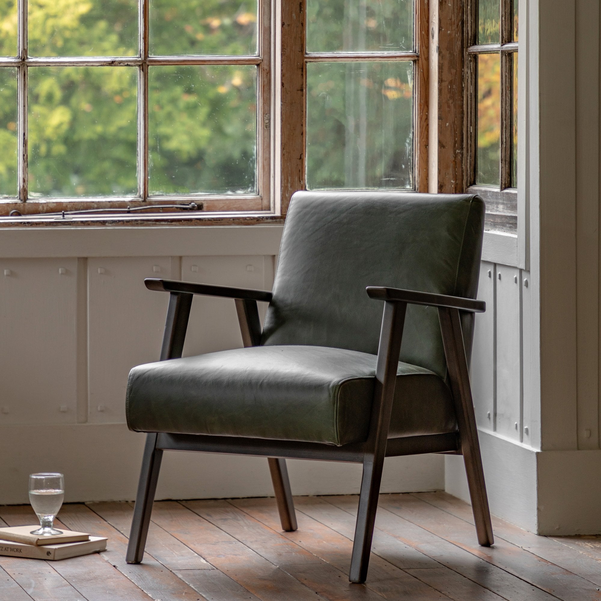 Green leather chair with wooden arms in front of a window overlooking trees.