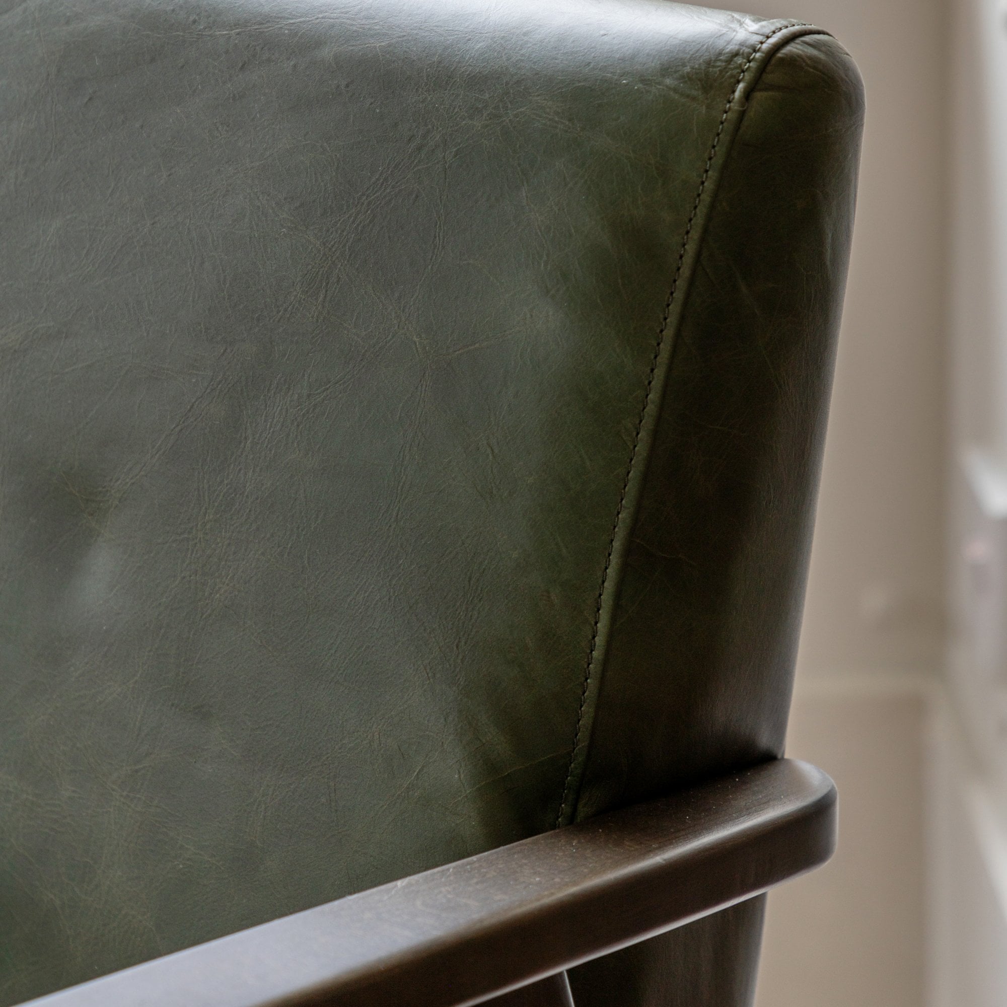 Close-up of the upper back and armrest of a green leather chair.