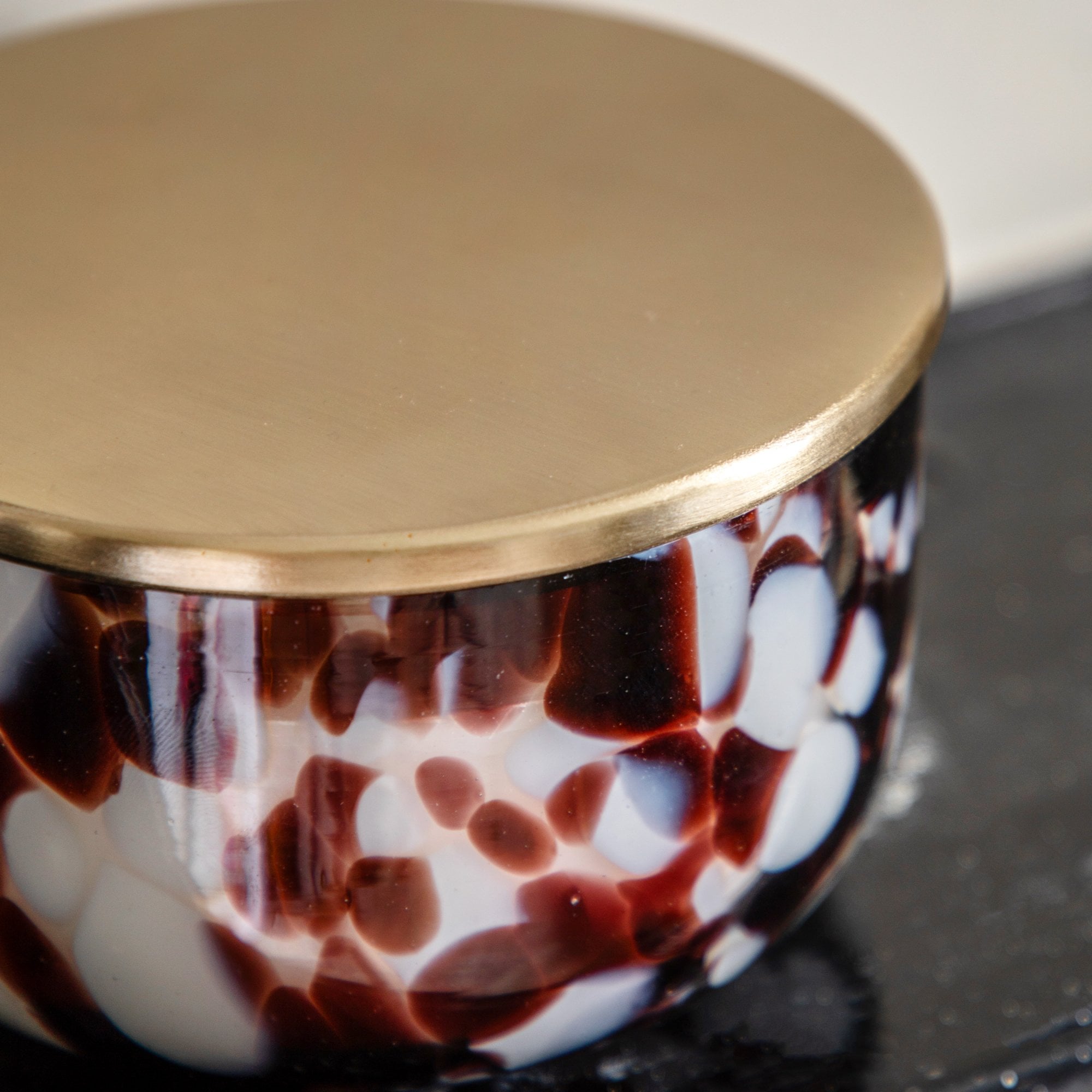 A short, wide glass candle in white with deep red and black splotches, lid on.