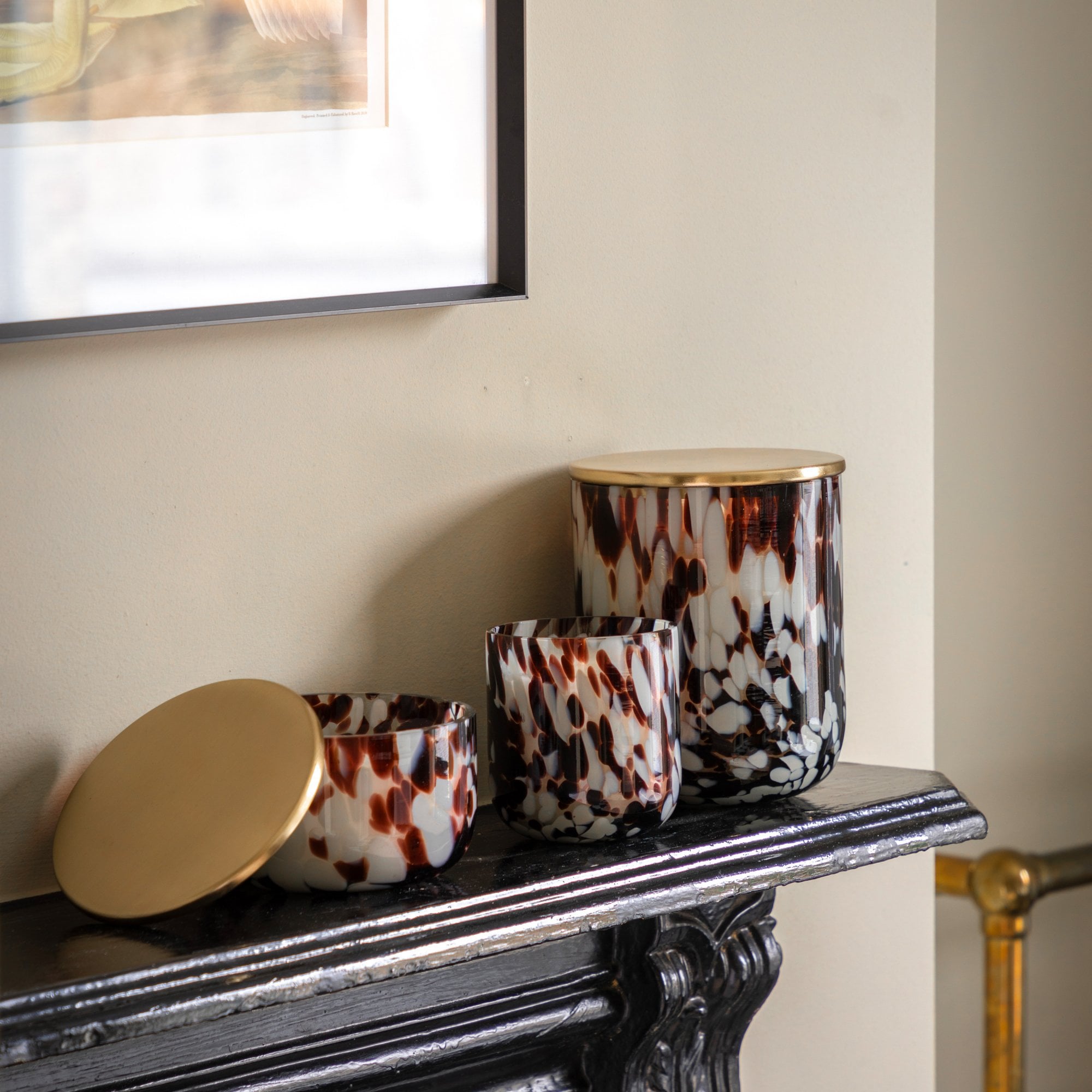 Three splotched candles in varying sizes on a mantel, one with its lid ajar.