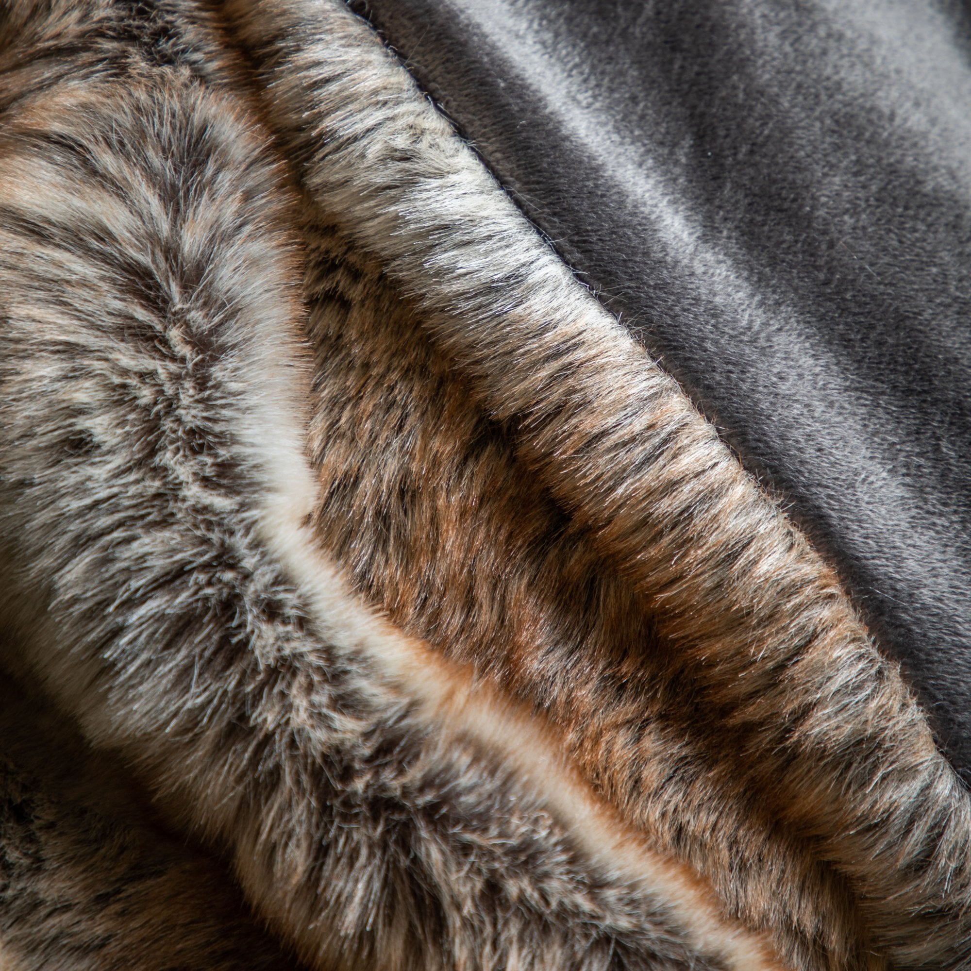 A close-up of the faux fur throw displaying its brown and cream texture next to a solid gray fabric.