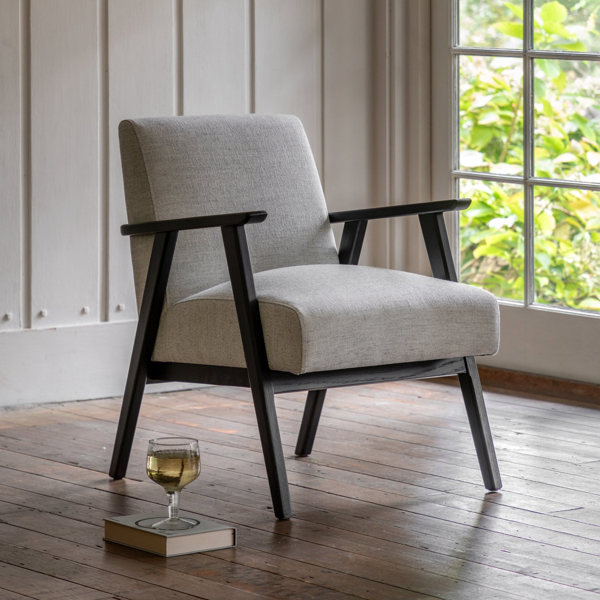 A mid-century style armchair with light grey upholstery and dark wooden frame in a sunlit room.