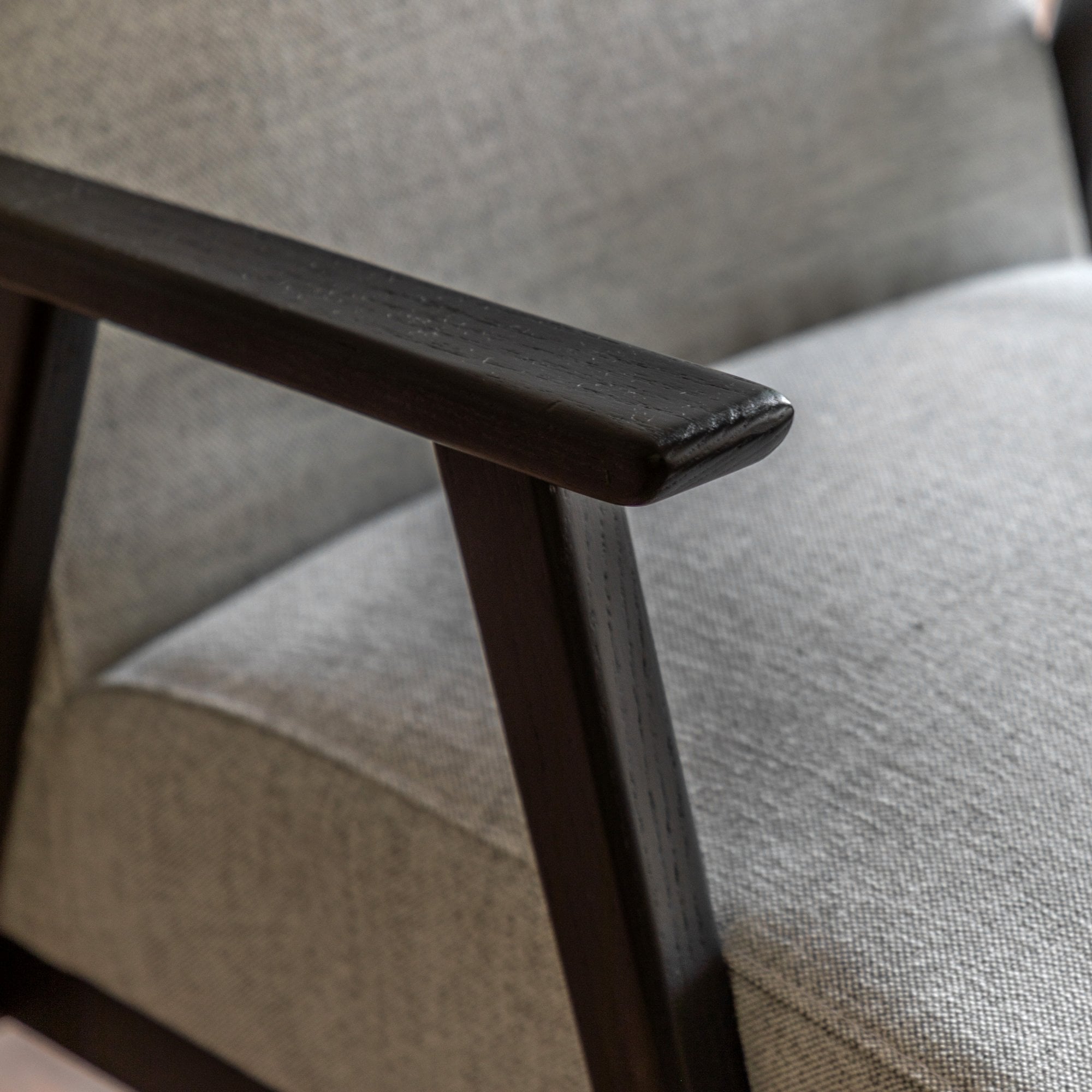Detail of the dark wooden armrest and the light grey fabric upholstery of the armchair.