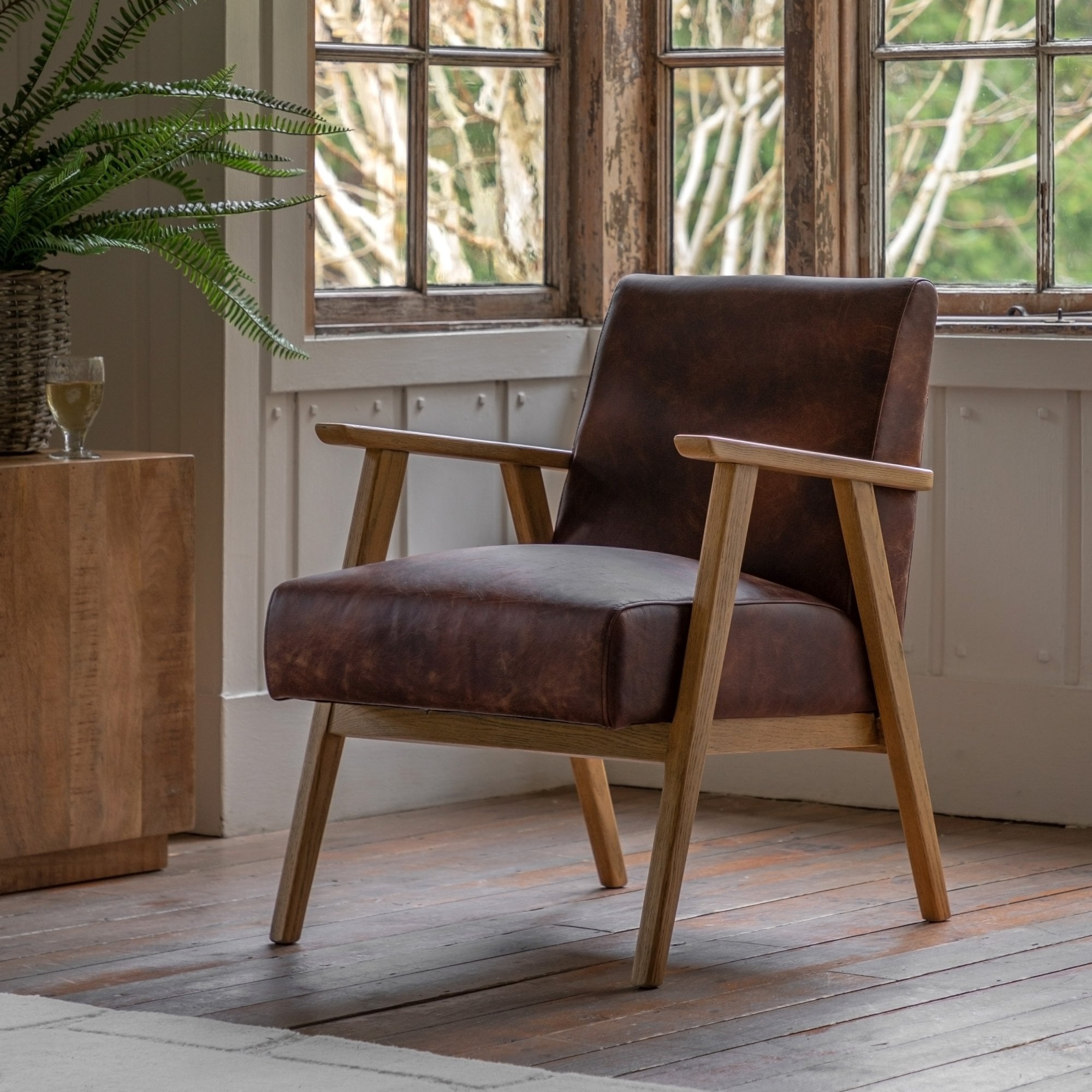 Brown leather armchair with wooden frame by a window with a fern plant.