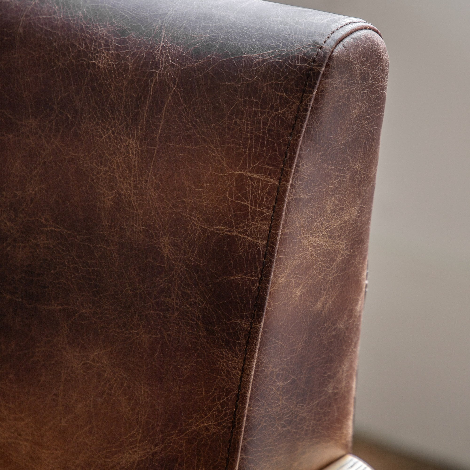 Close-up of the distressed brown leather upholstery on the armchair backrest.