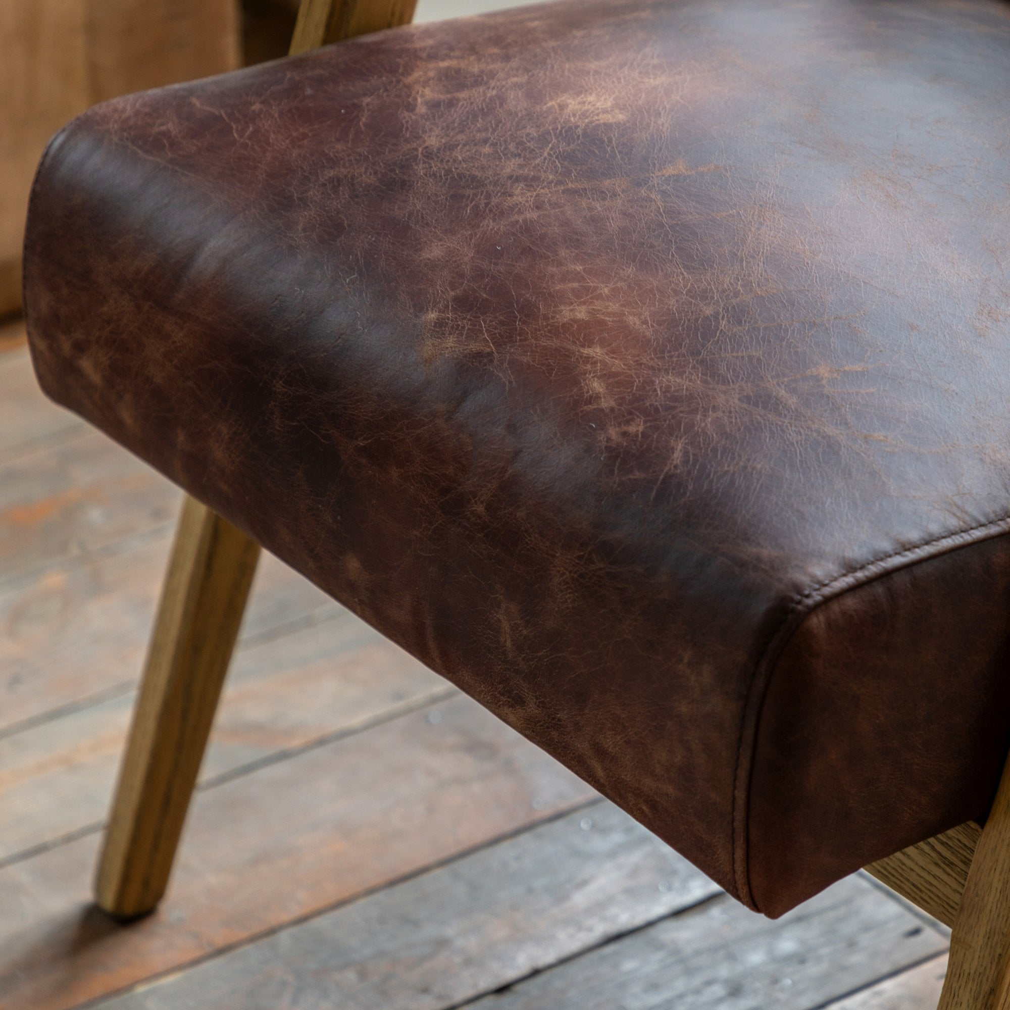 Detailed view of the brown leather seat cushion and wooden frame of the armchair.