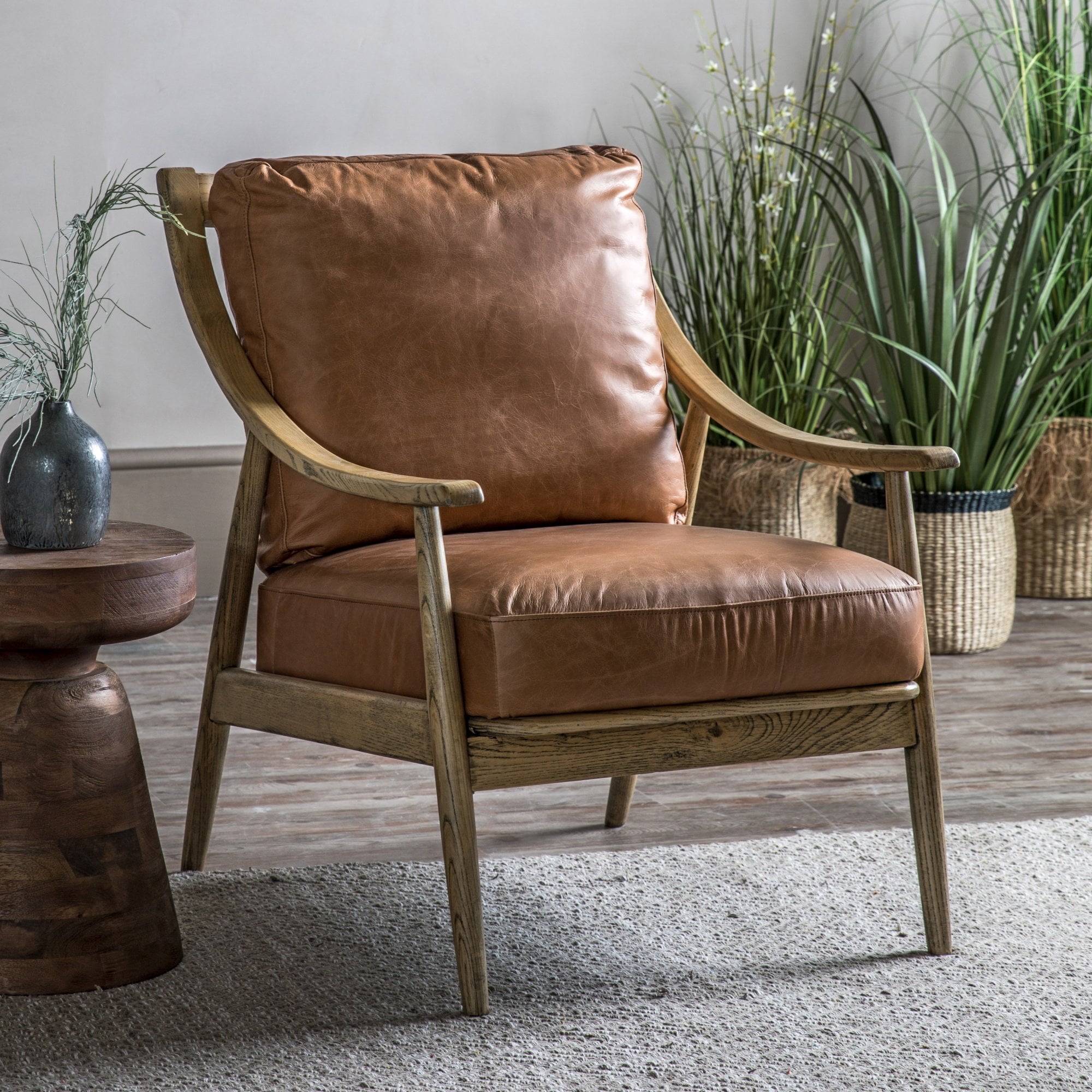 Stylish brown leather armchair with a wooden frame in a living room setting with plants.