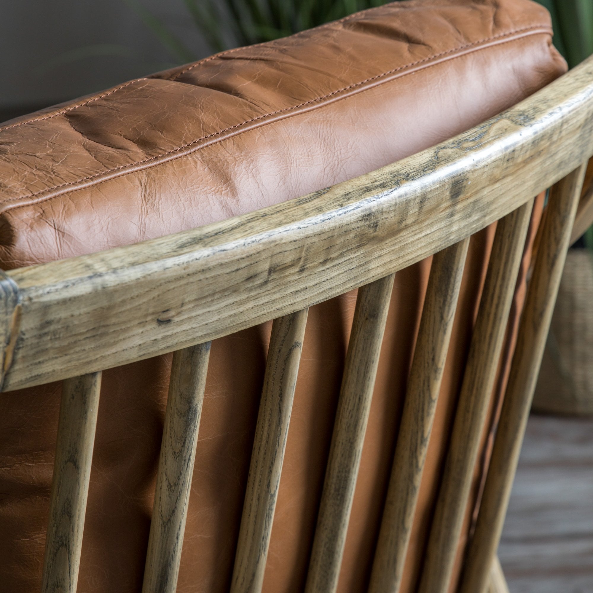 Close-up of the back of a brown leather armchair, showing wooden spindle details.