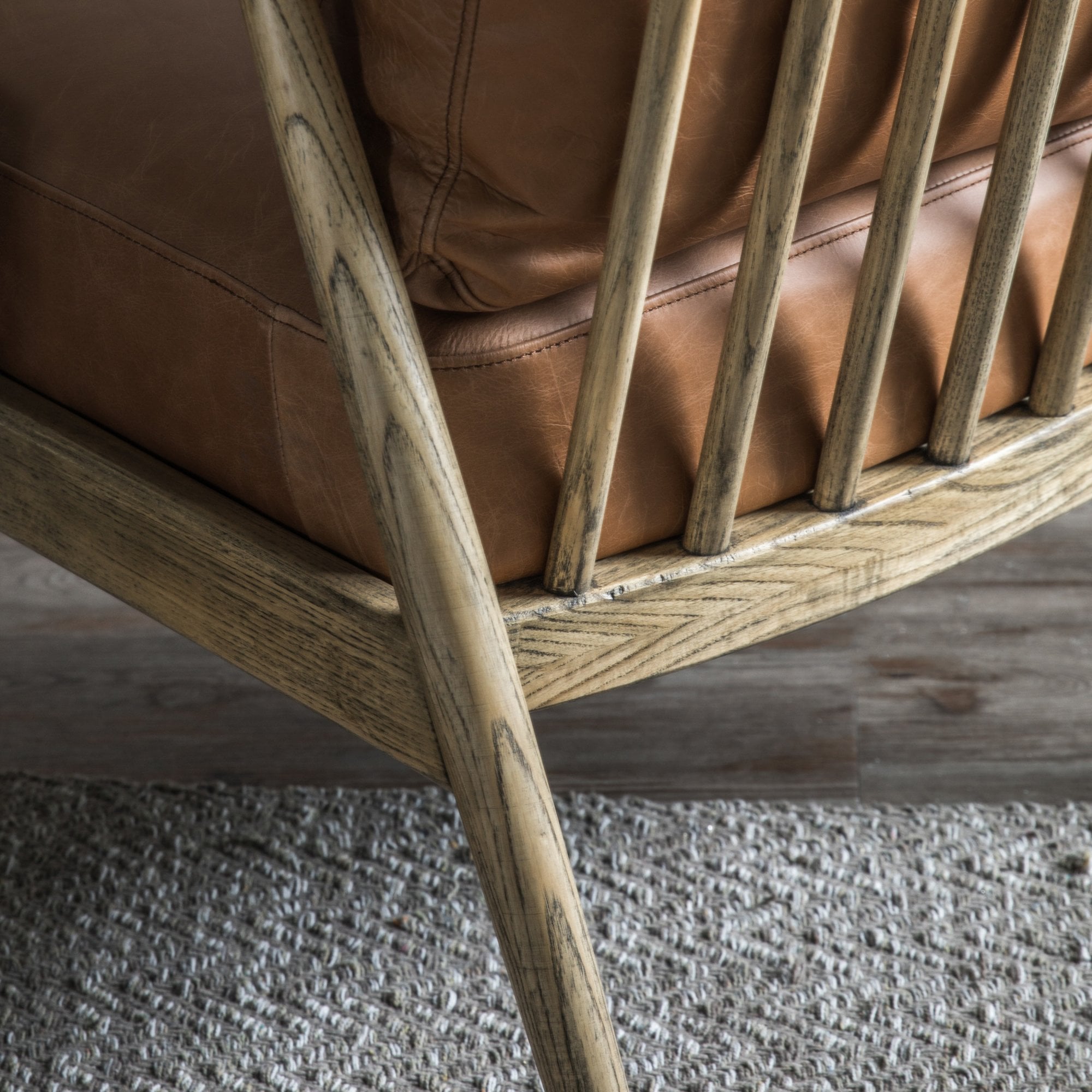 Close-up of the wooden leg and frame of a brown leather armchair on a rug.