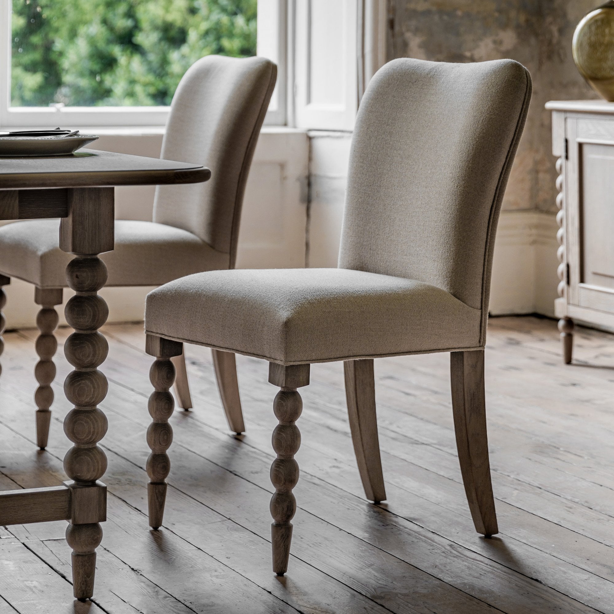 Two upholstered dining chairs with rounded front legs next to a dining table.