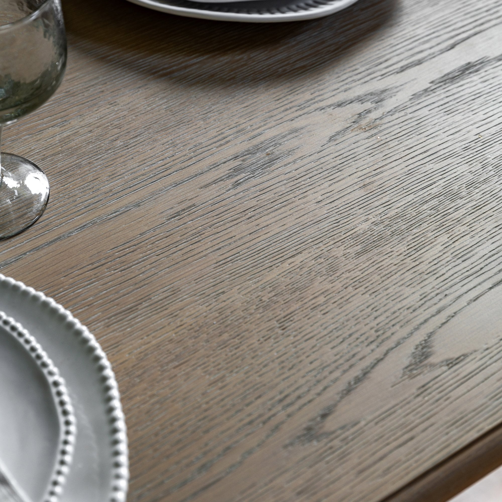 Close-up of the light wood grain surface of a dining table with plates and glasses.