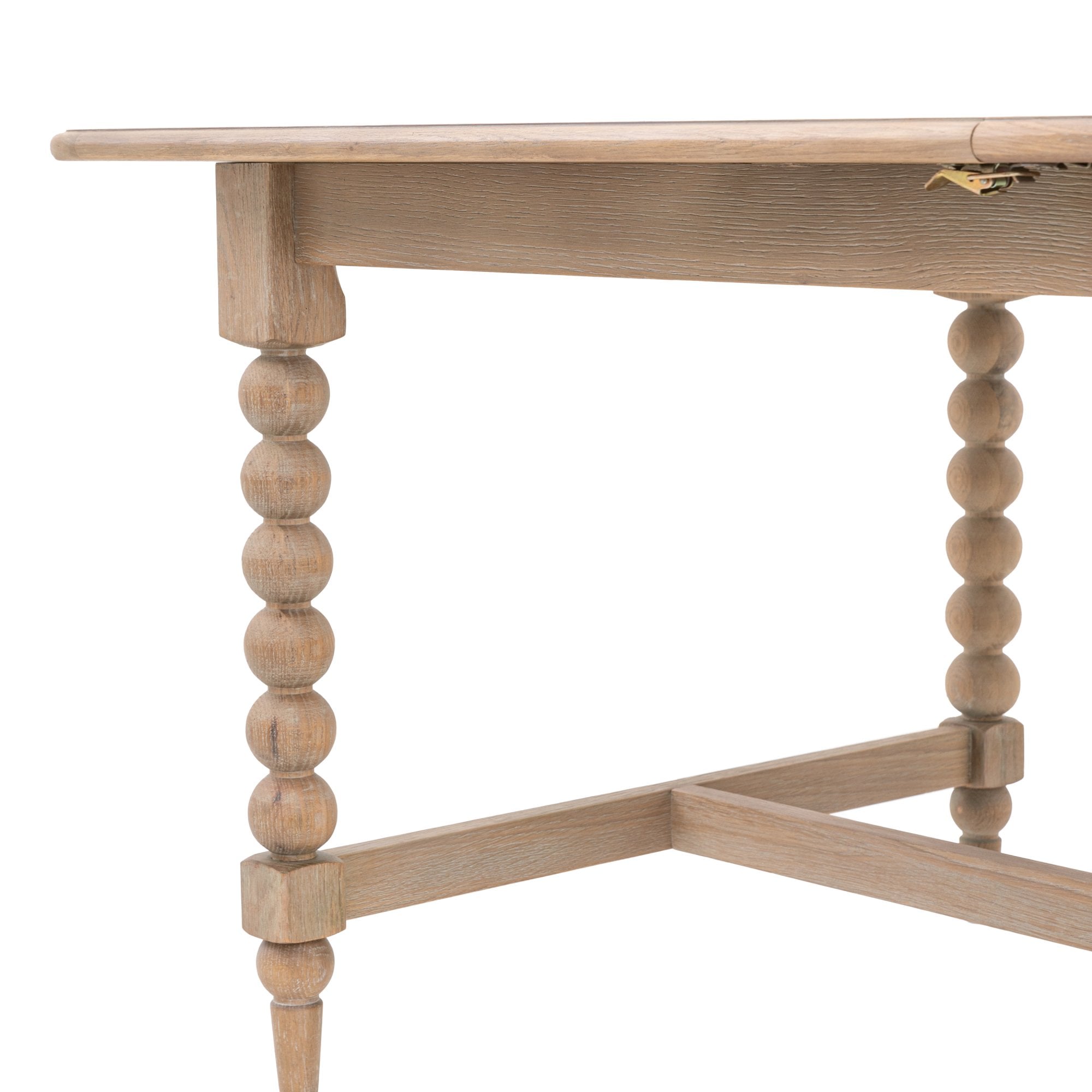 Close-up of the corner of a light wood dining table with a bobbin leg and crossbar.