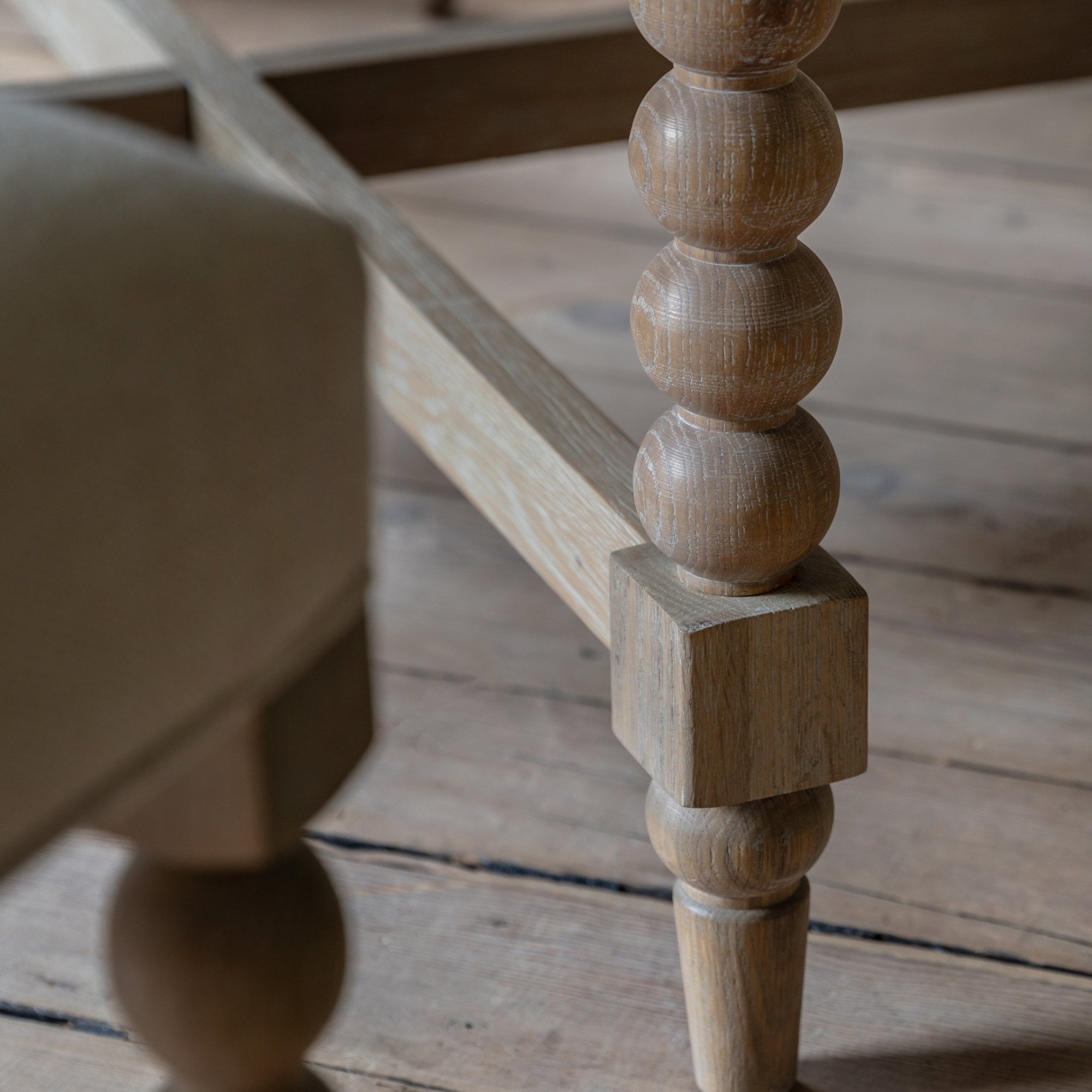 Close-up of a decorative turned wood table leg on a wooden floor.