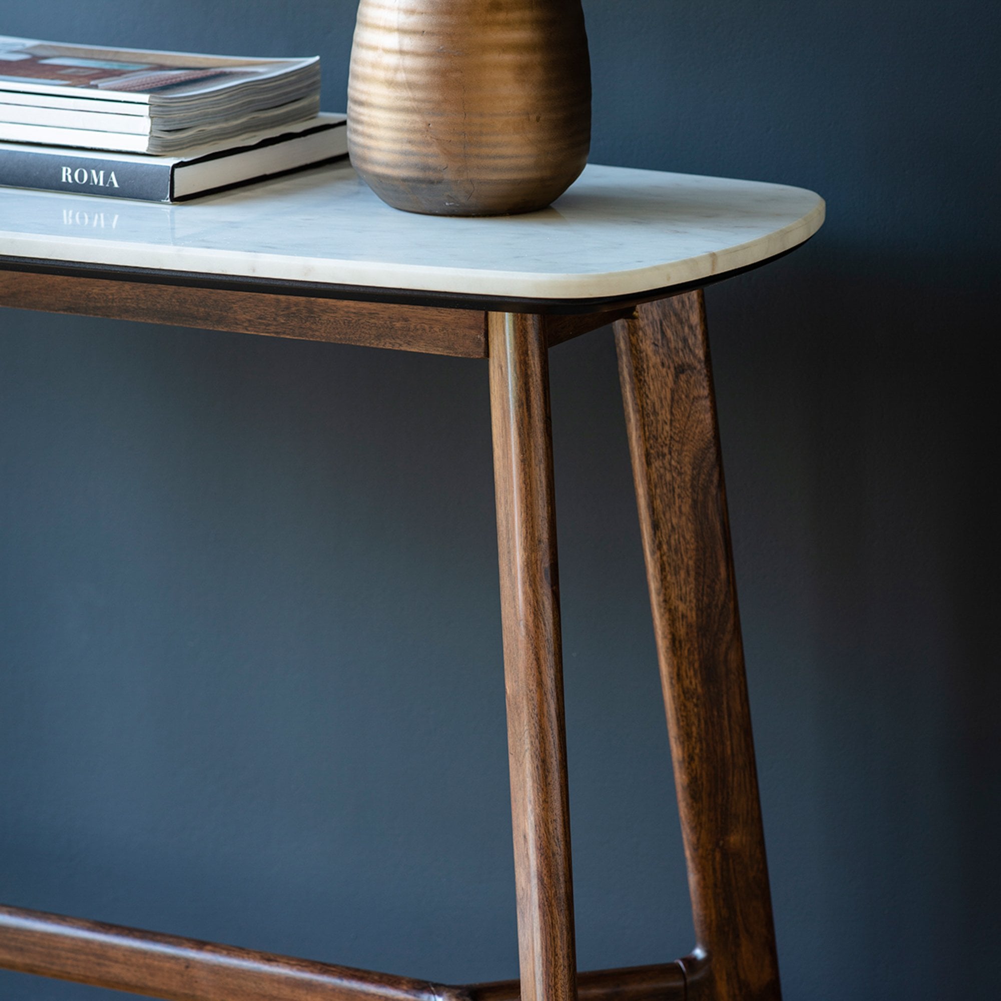 A closeup of a console table with a white marble top and dark wooden legs.