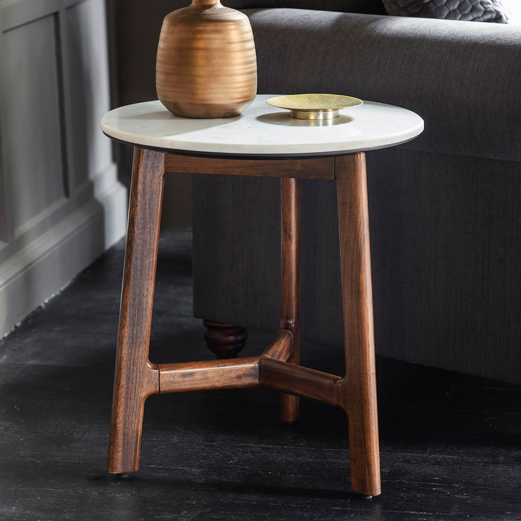 Round white marble top side table with wooden base and a brown vase and gold bowl on top.