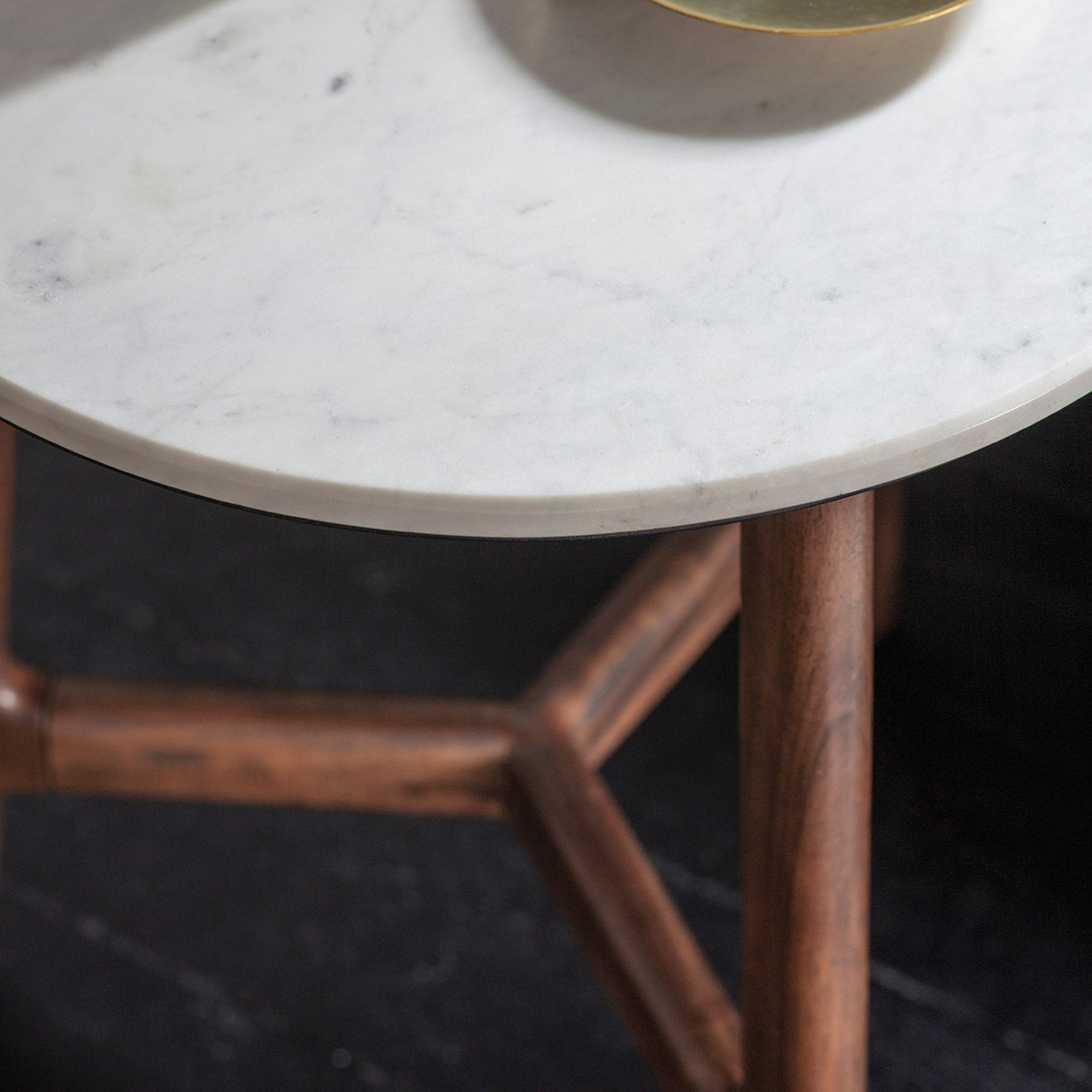 Close-up of the round white marble top and dark wooden legs of a side table.