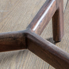 Close-up of the dark wooden, tripod-style base of a side table on a wooden floor.