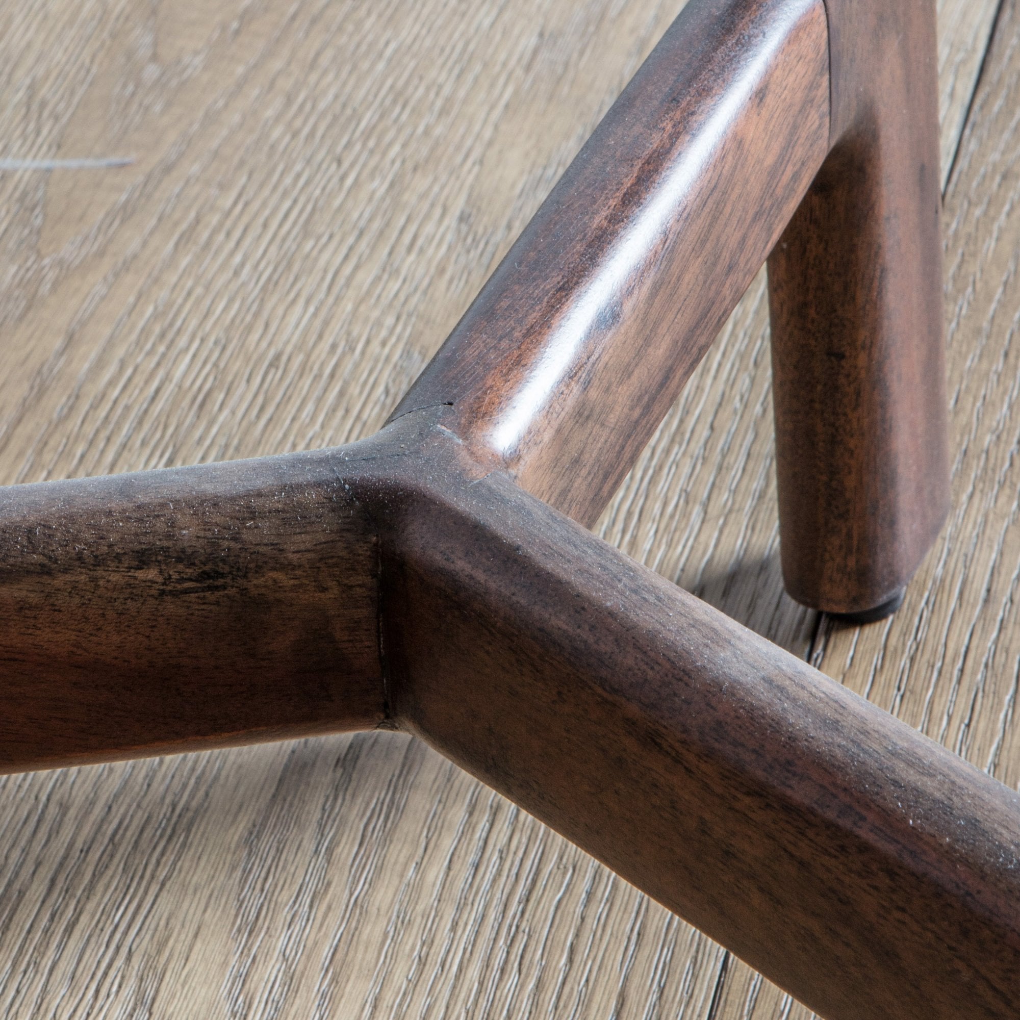 Close-up of the dark wooden, tripod-style base of a side table on a wooden floor.