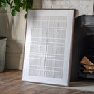 A framed piece of wall decor is leaning against a wall and next to a fireplace.
